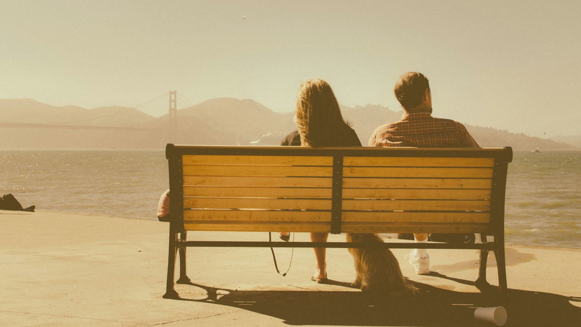 man and woman sitting on bench beside body of water