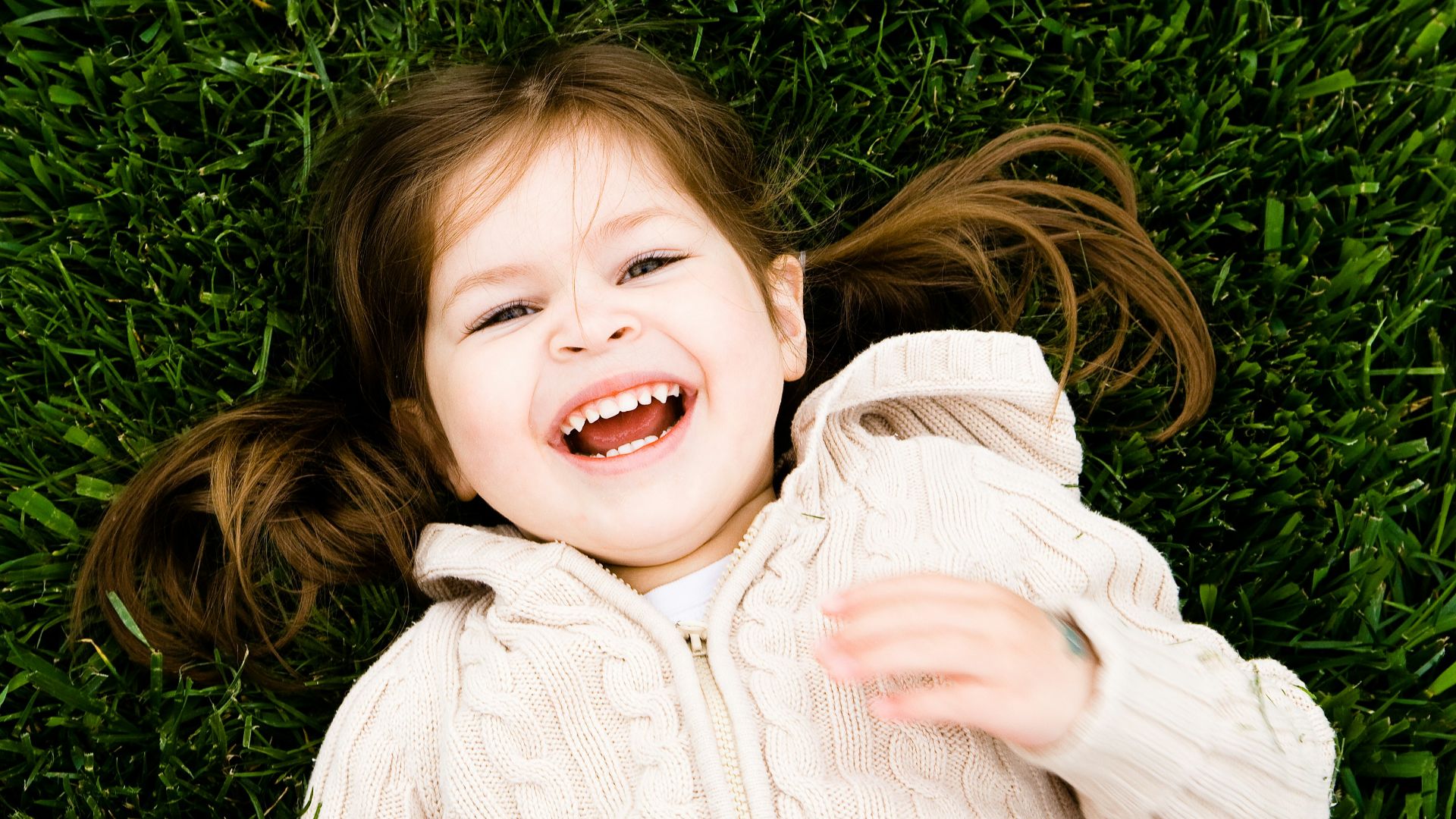 girl smiling while lying on grass field at daytime