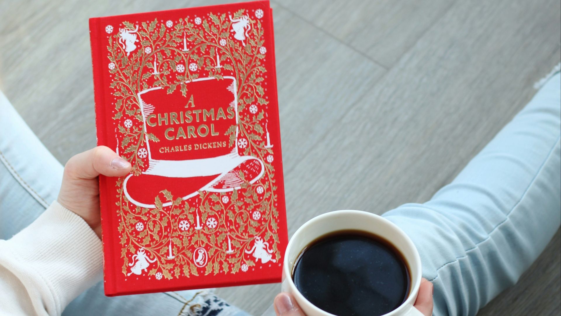 a person holding a red christmas card next to a cup of coffee