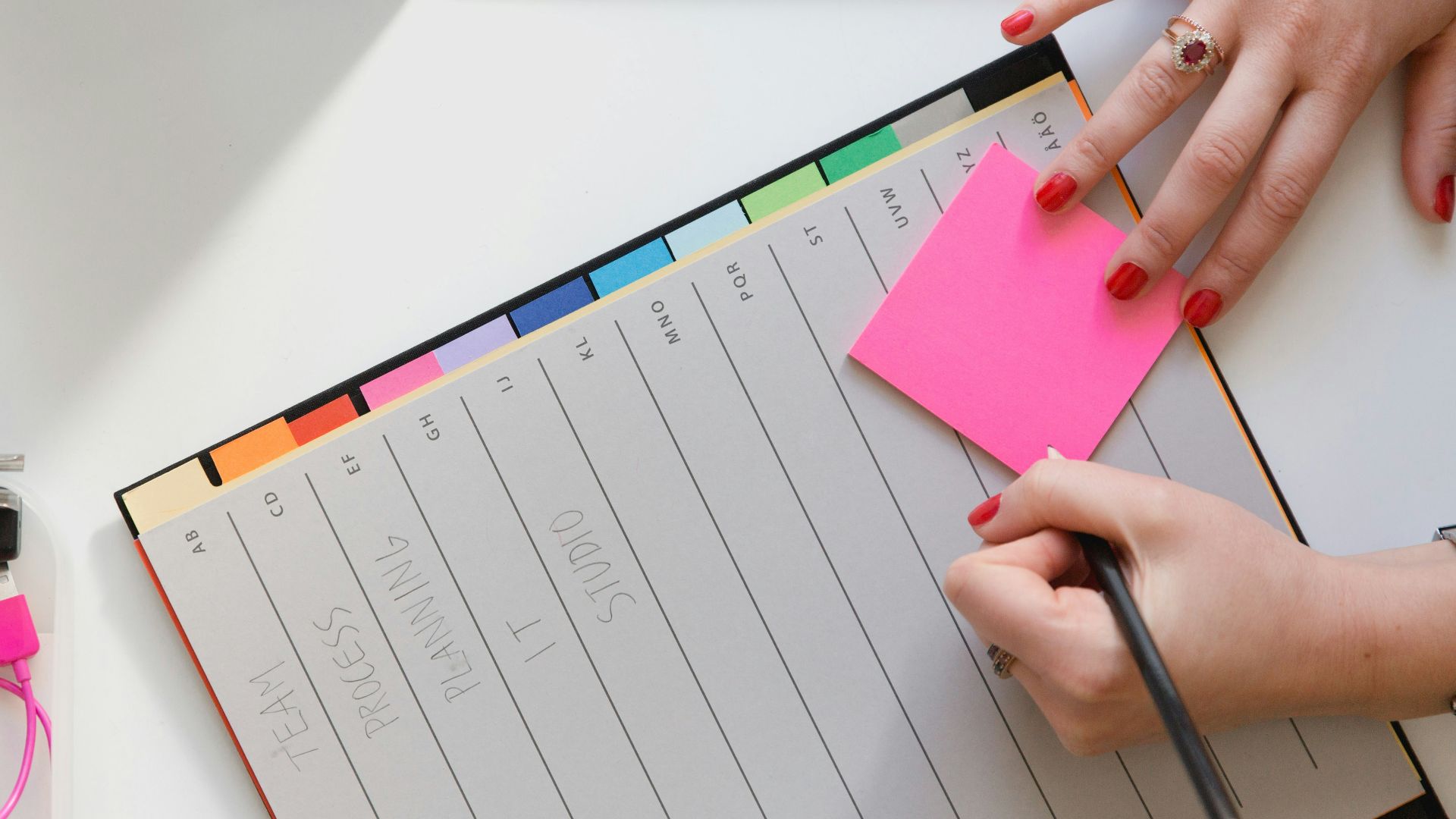 person holding pencil and stick note beside table