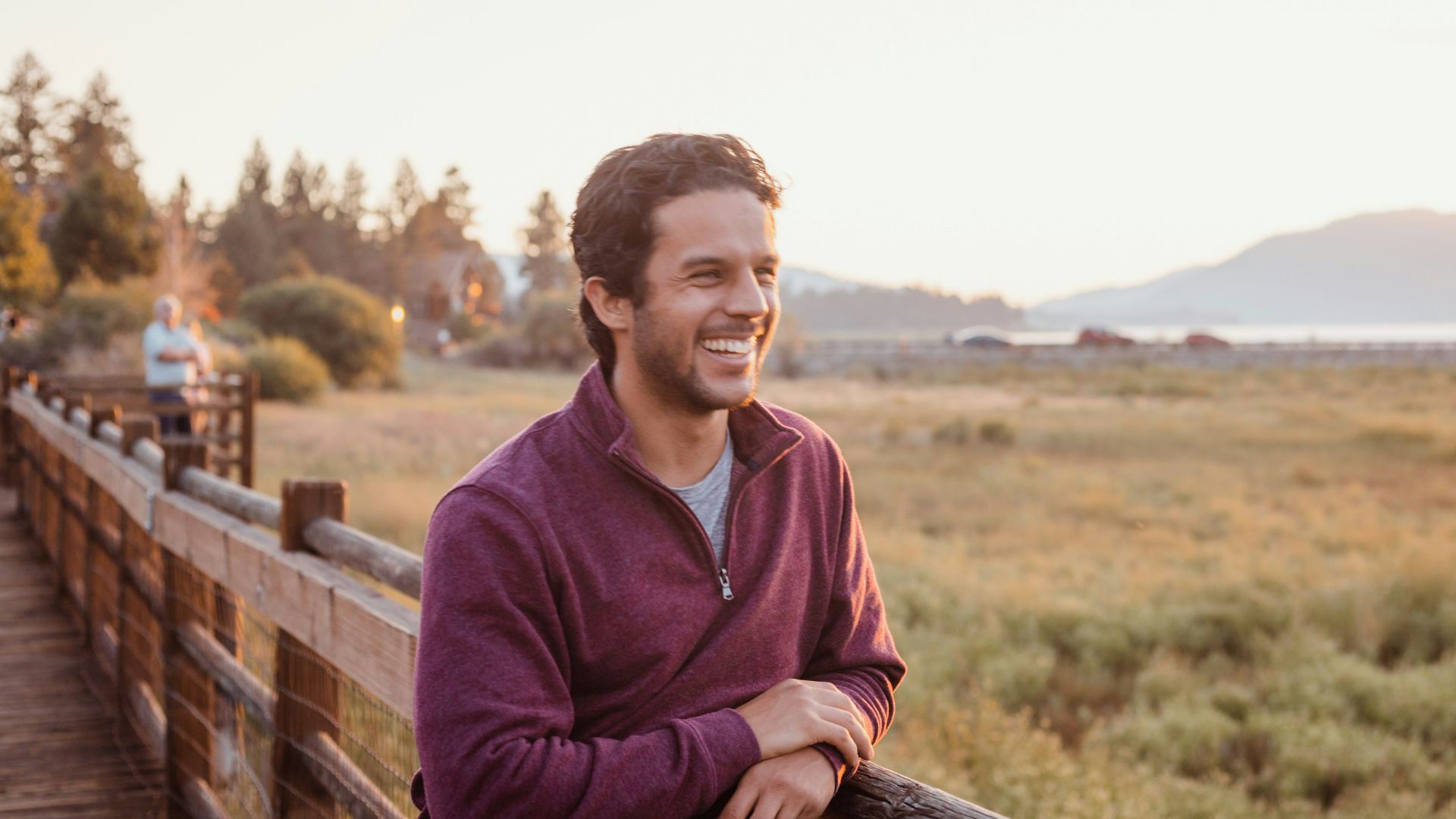 man in purple hoodie sitting on brown wooden fence during daytime