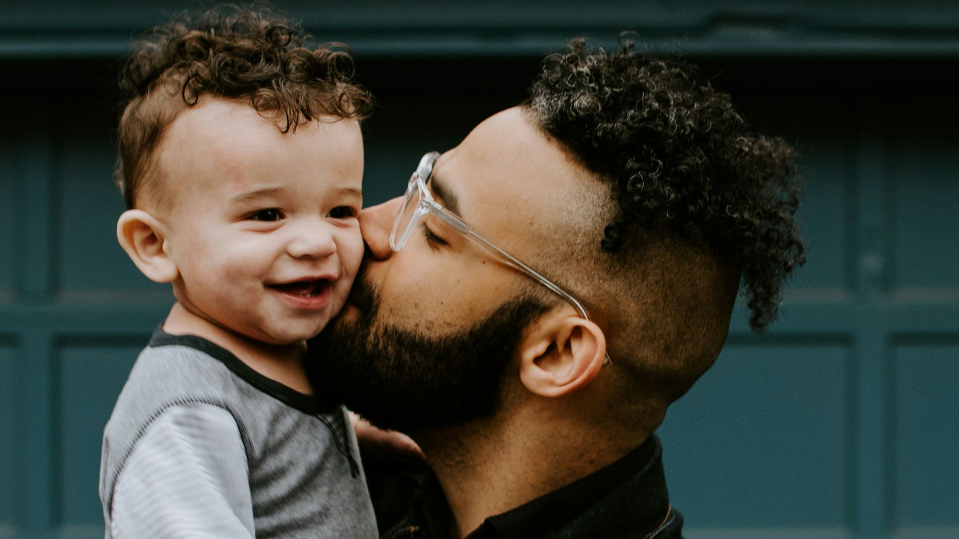 man carrying baby boy and kissing on cheek