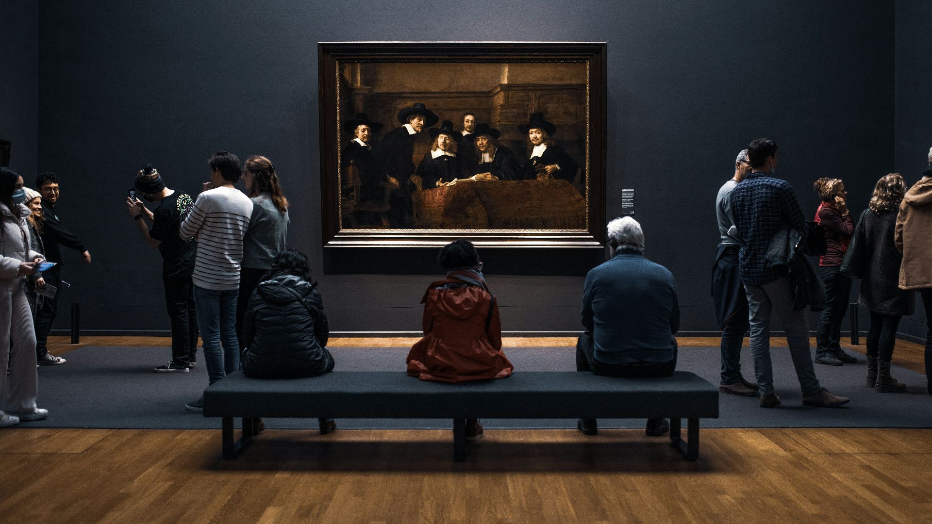 a group of people standing around a museum looking at a painting