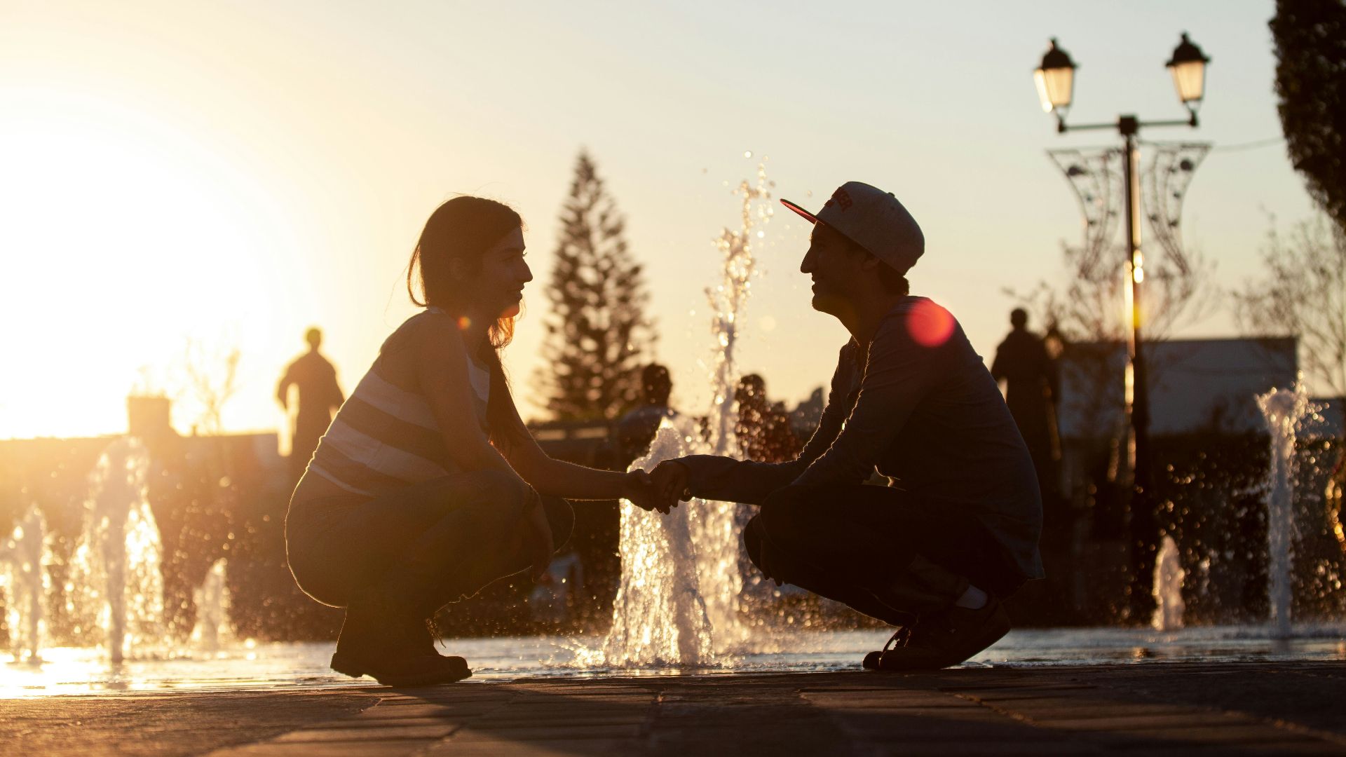 man and woman sitting on water fountain during sunset