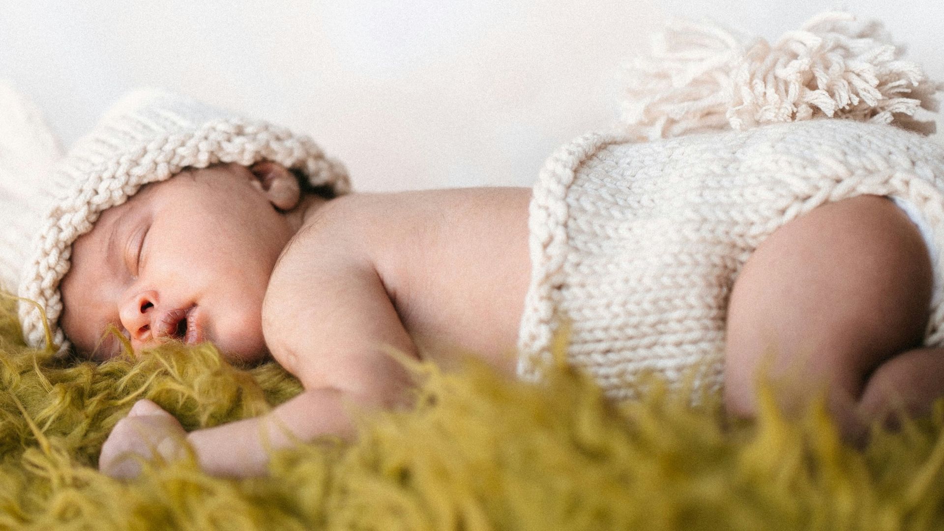 baby in white knit cap lying on green textile