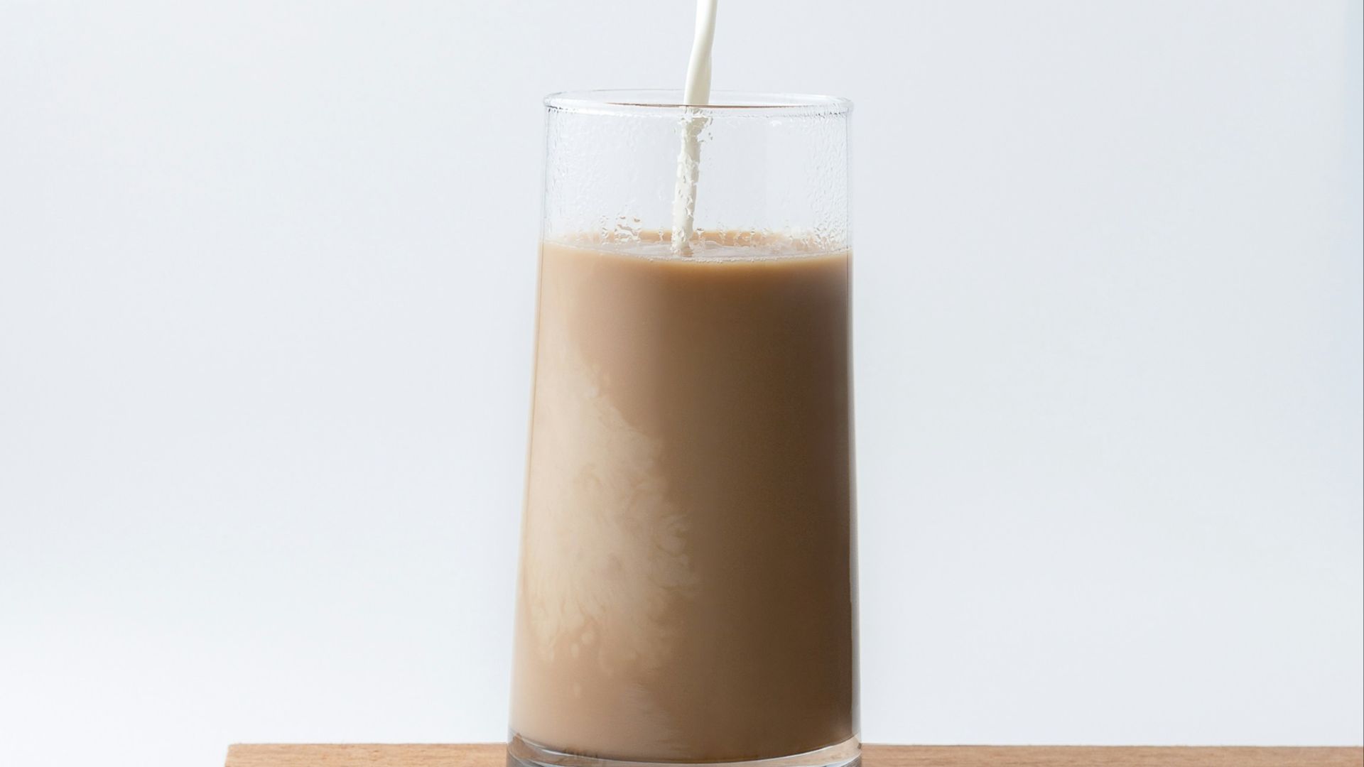 person pouring milk into chocolate filled glass cup