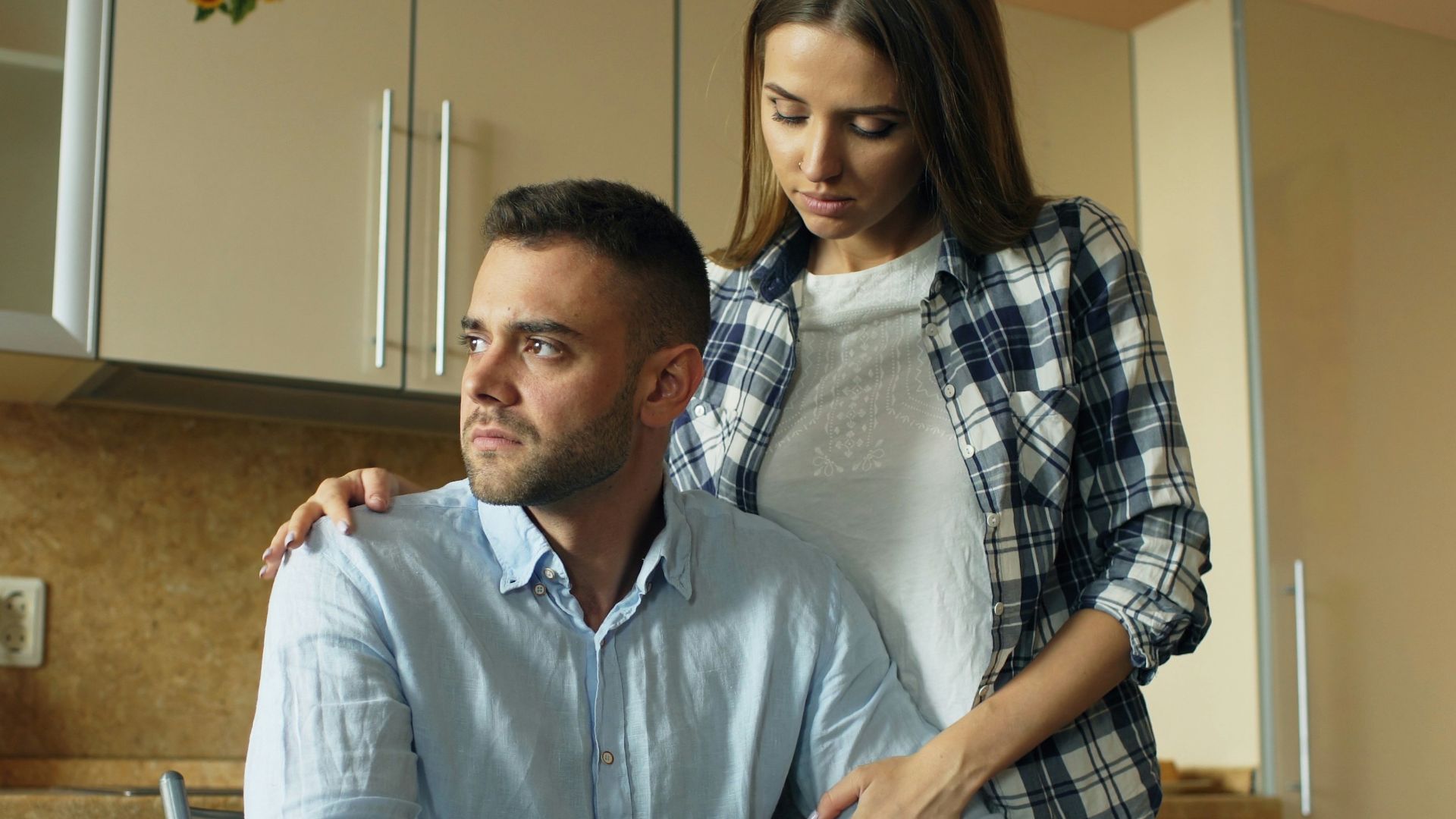 Woman comforts man at kitchen table with food.