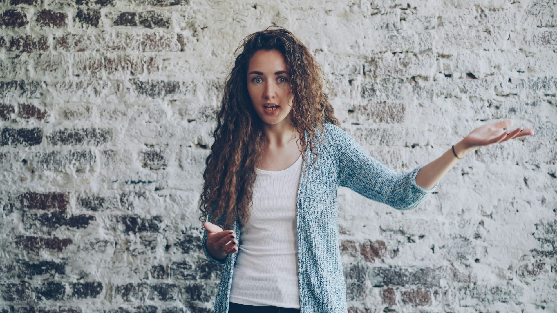Woman gesturing while speaking against brick wall.