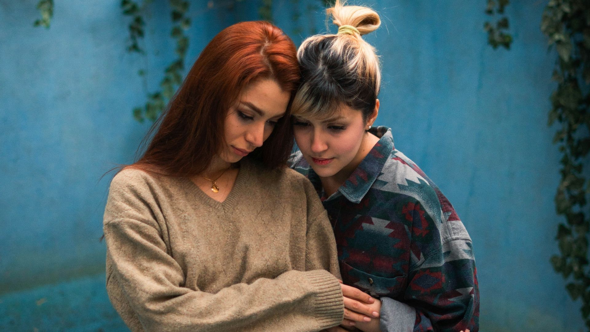 Two women embracing against a blue wall.