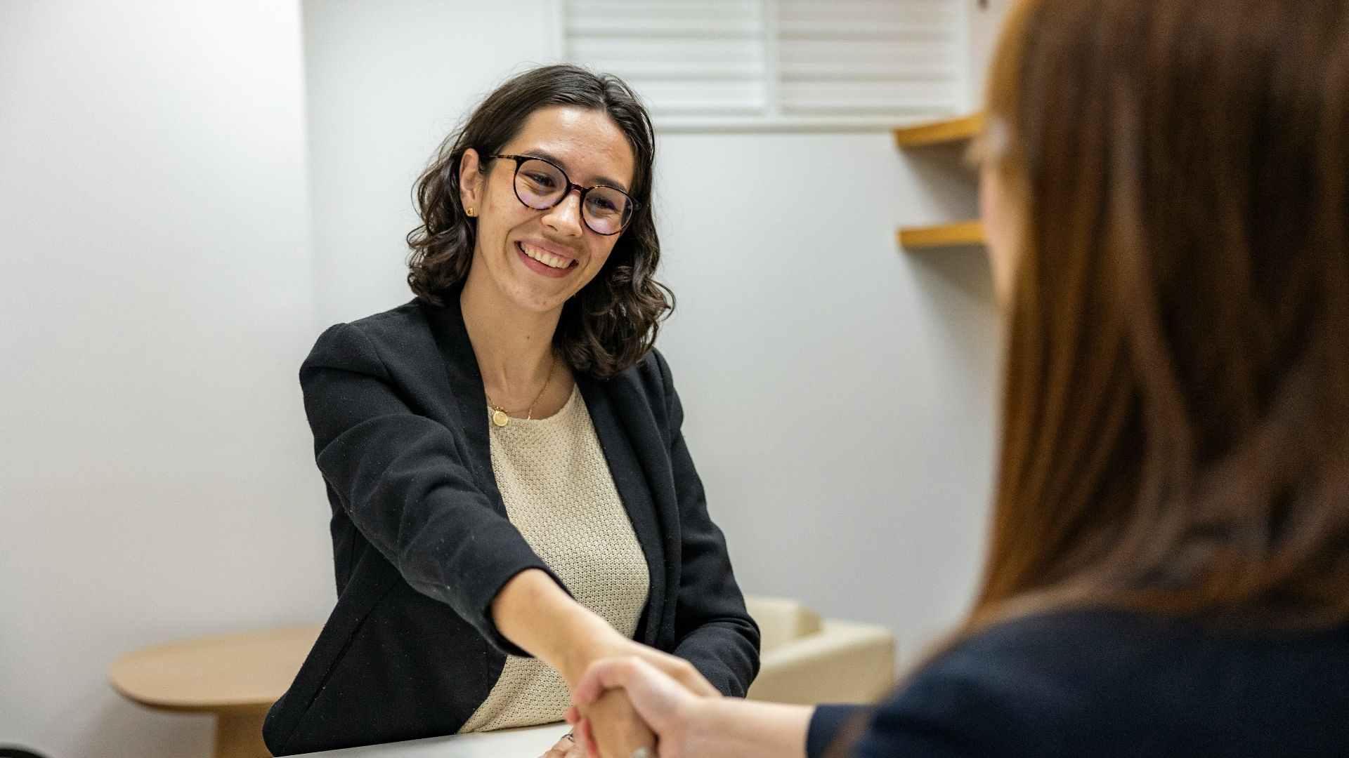 a woman shaking hands with another woman sitting at a table