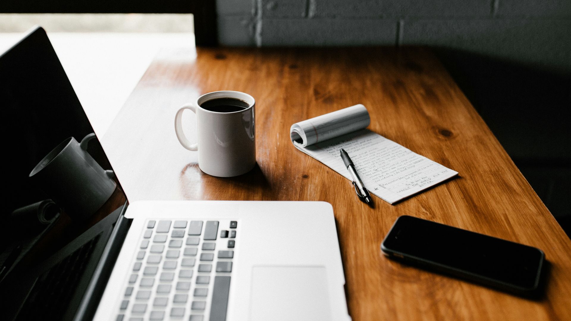 MacBook Pro, white ceramic mug,and black smartphone on table