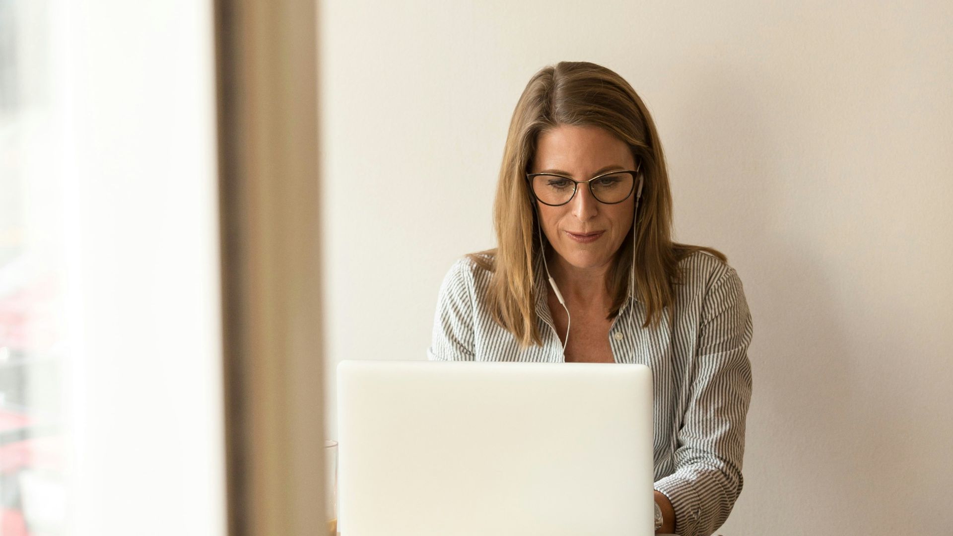 woman wearing grey striped dress shirt sitting down near brown wooden table in front of white laptop computer
