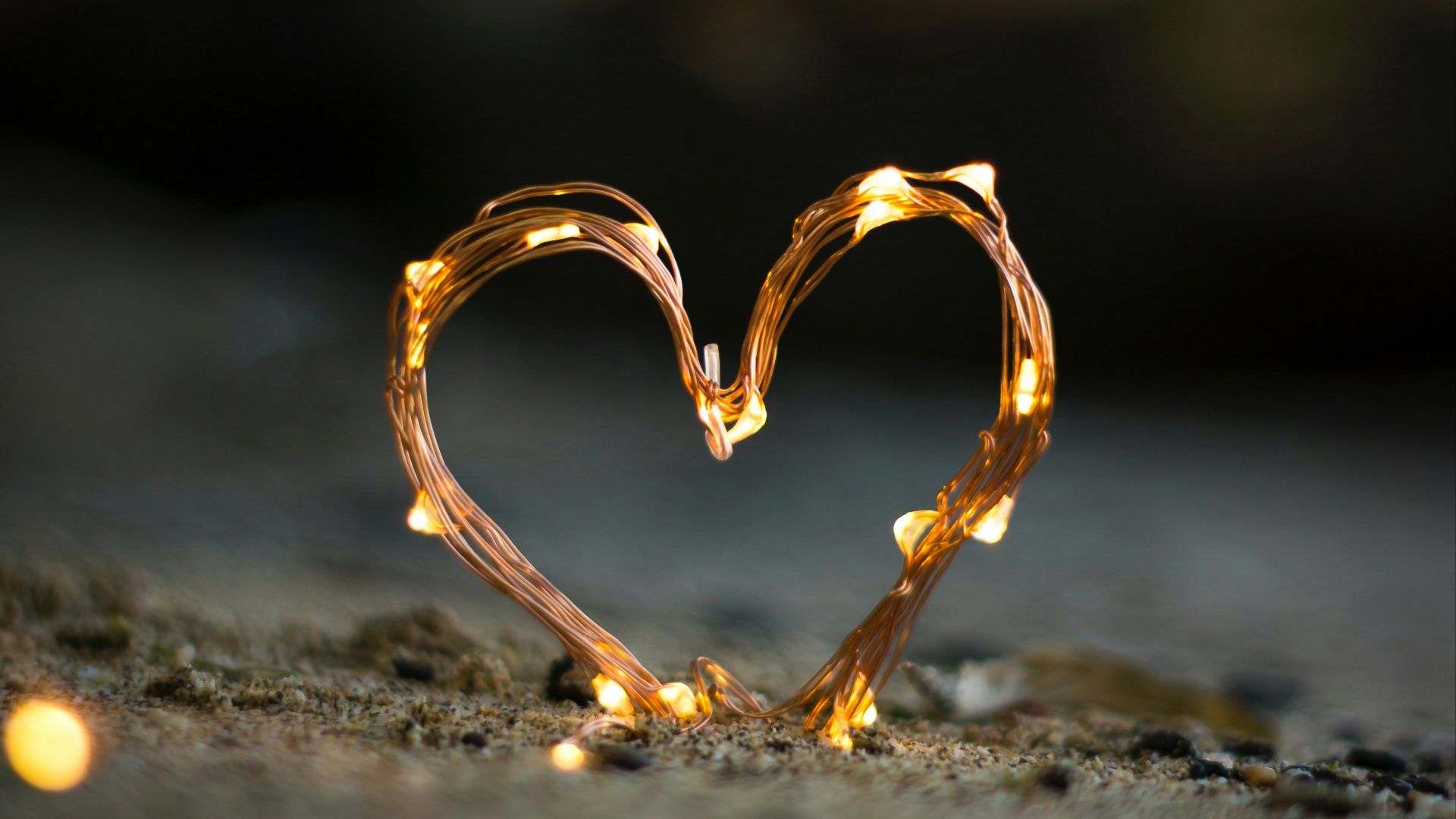 close-up photography of heart shaped fairy lite on brown sand