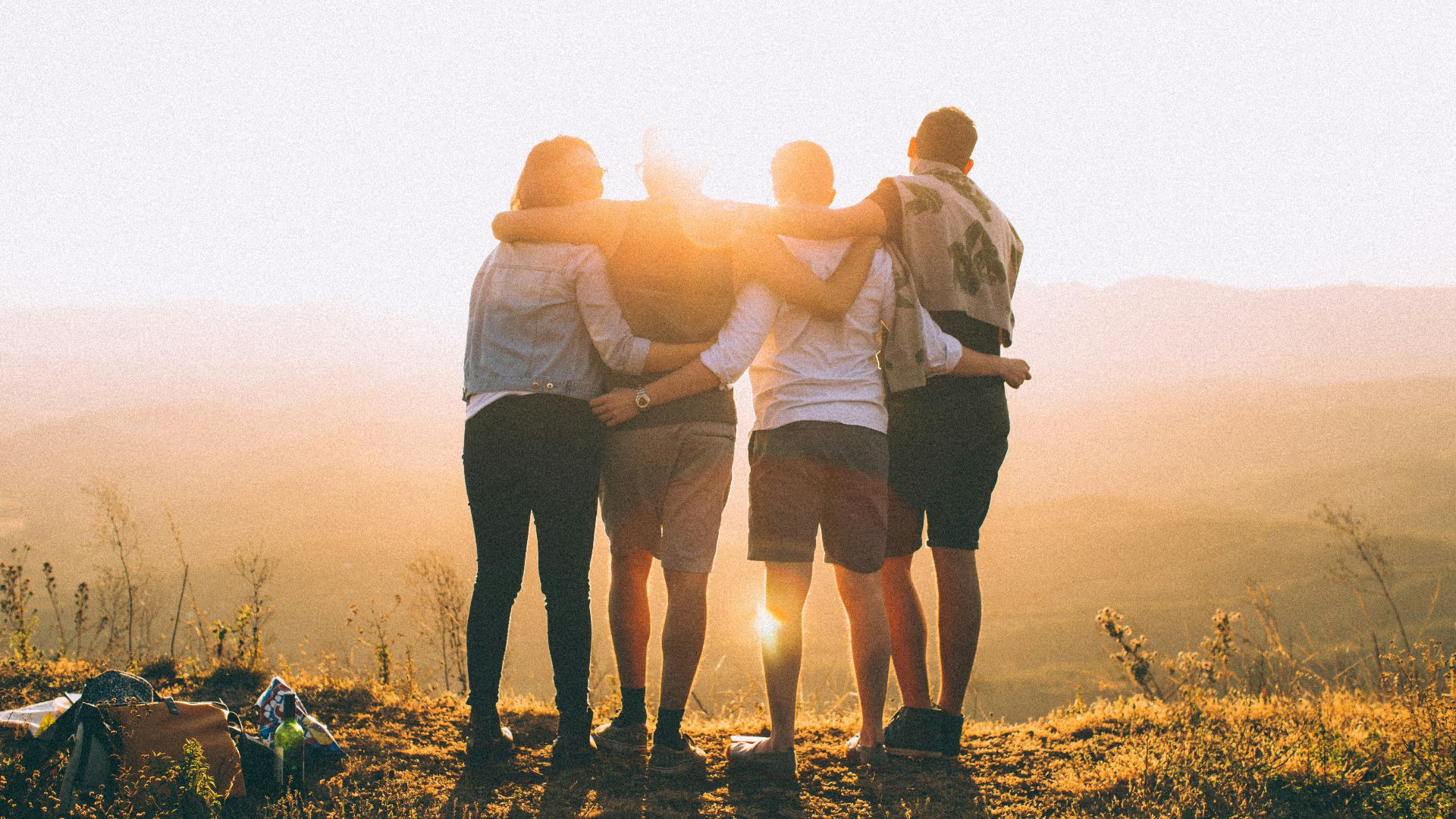 four person hands wrap around shoulders while looking at sunset