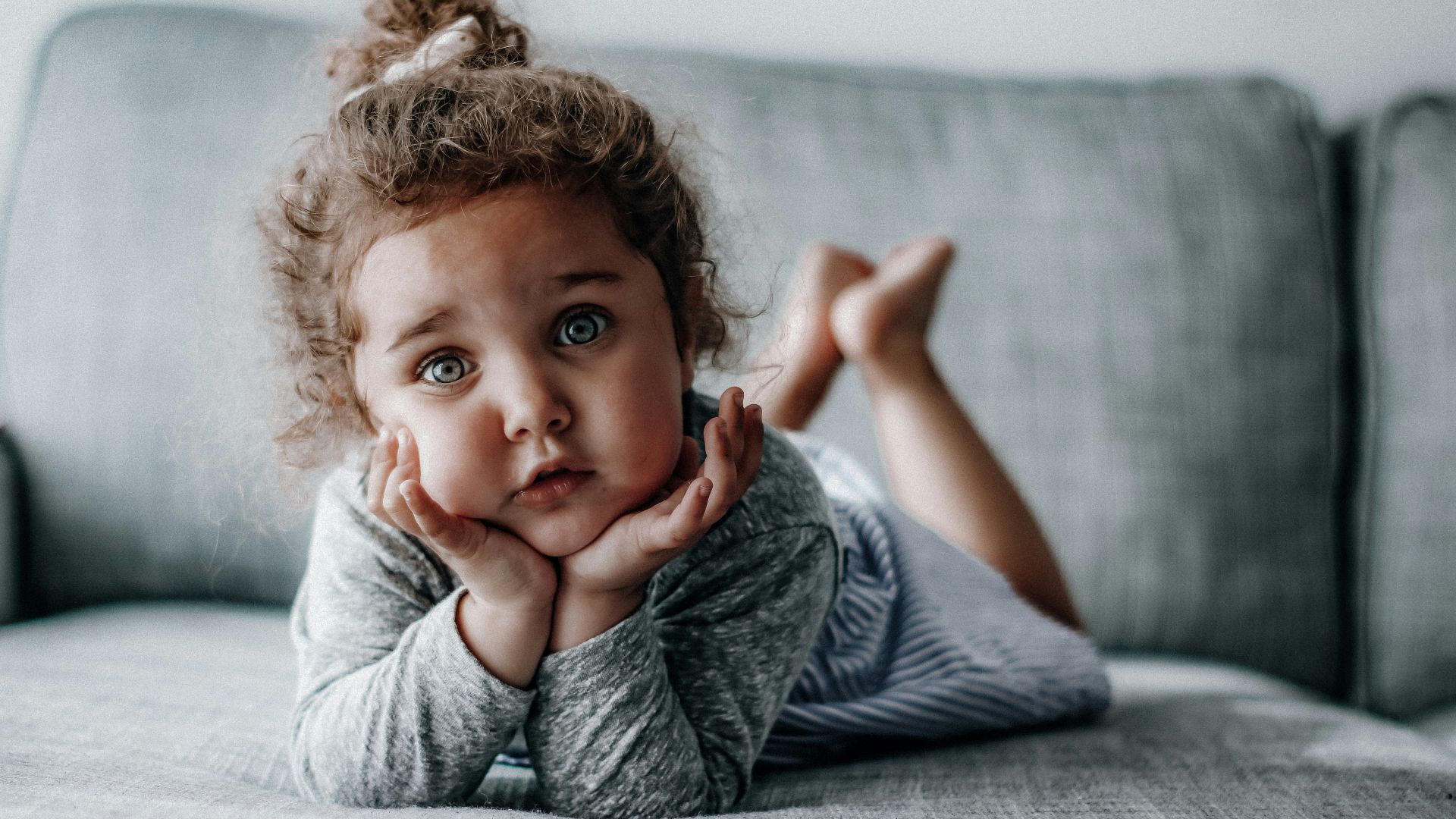 girl in gray long sleeve shirt lying on gray textile