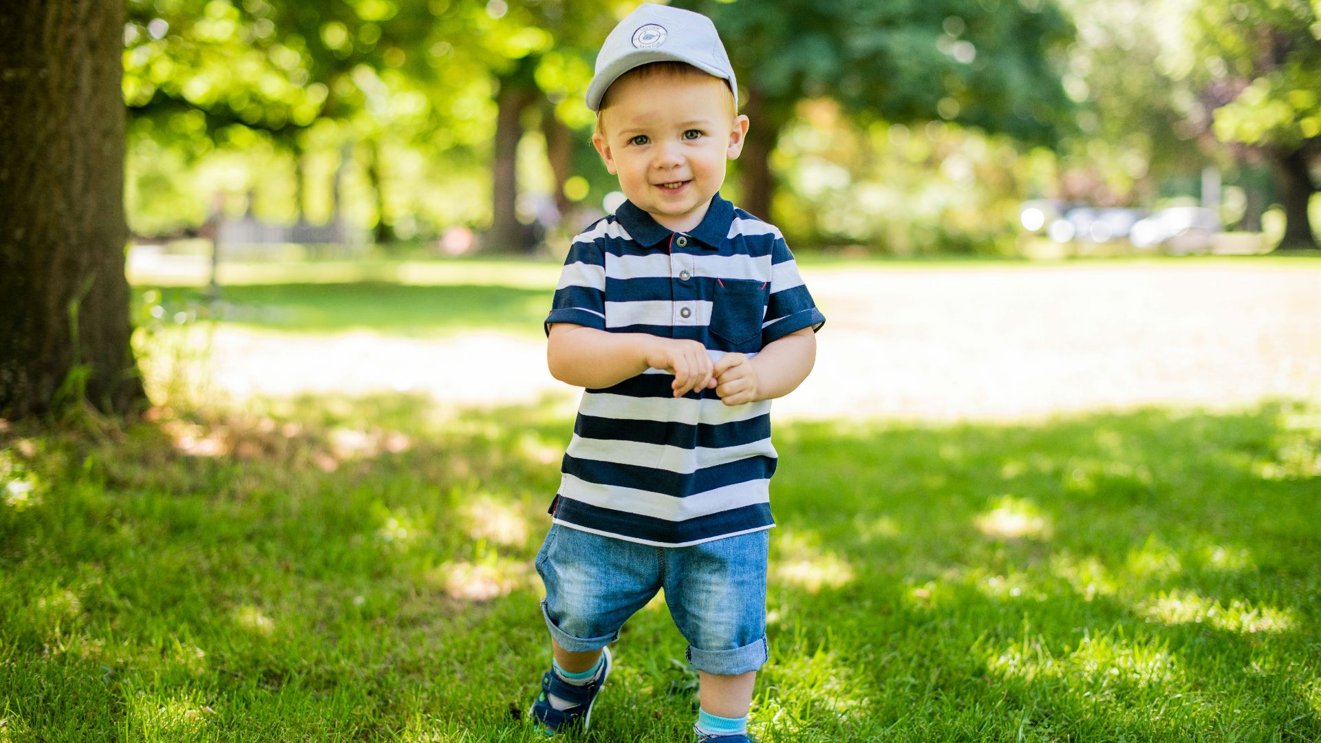 boy in black and white stripe polo shirt and blue denim shorts standing on green grass