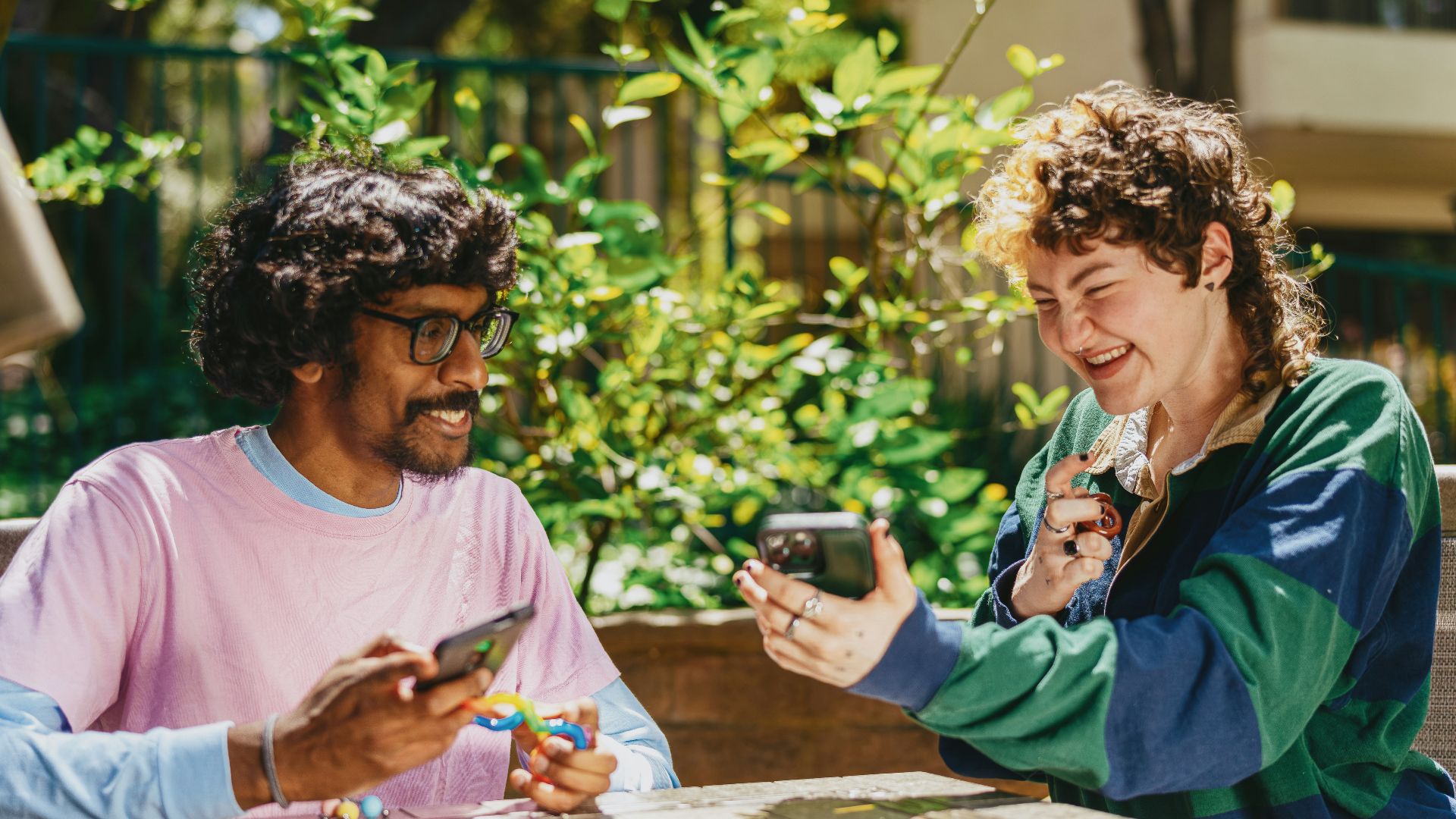 Two autistic friends sitting outside using stim toys and laughing at their phones