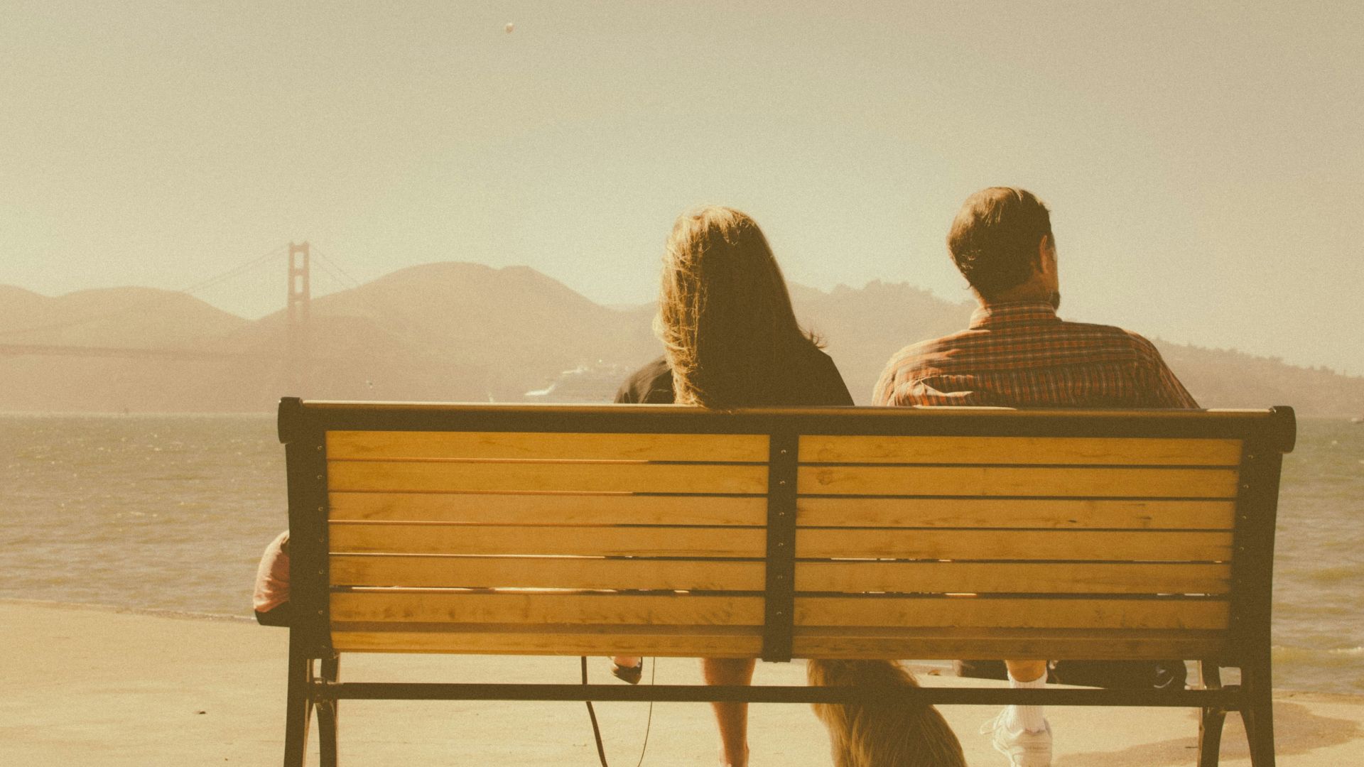 man and woman sitting on bench beside body of water
