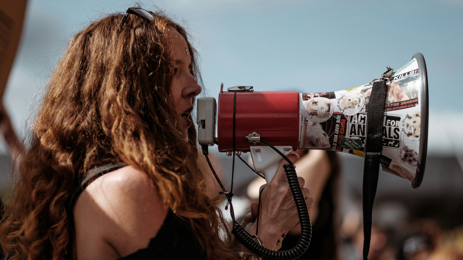selective focus photography of woman wearing black cold-shoulder shirt using megaphone during daytime