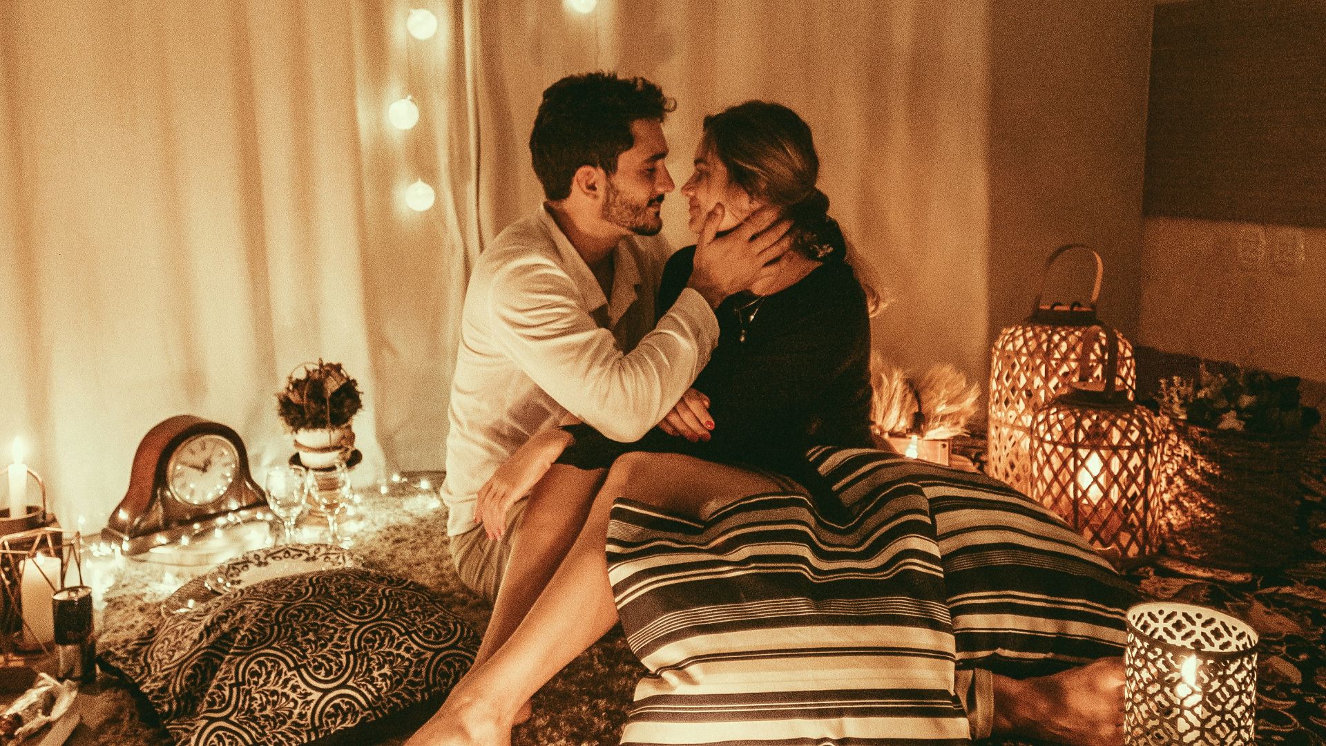 man and woman sitting on floor and about to kiss with lighted candles inside room