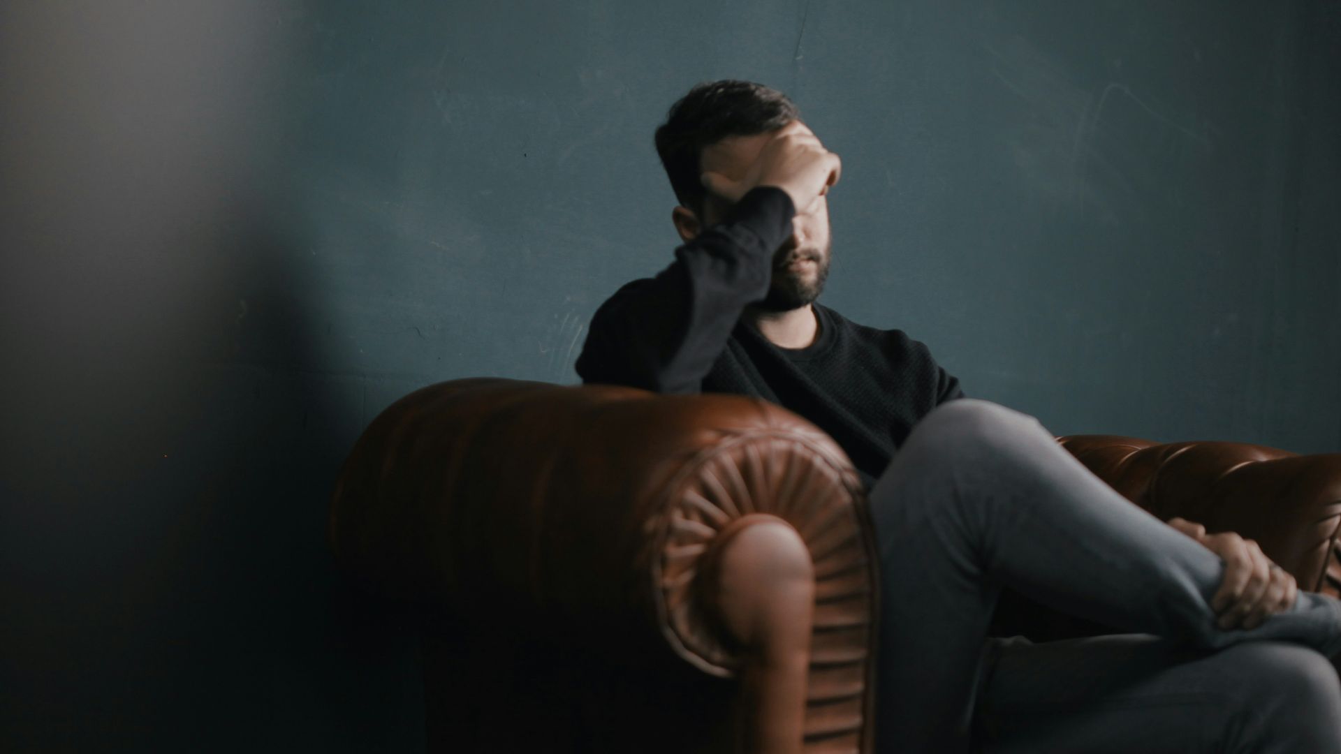 a man holds his head while sitting on a sofa