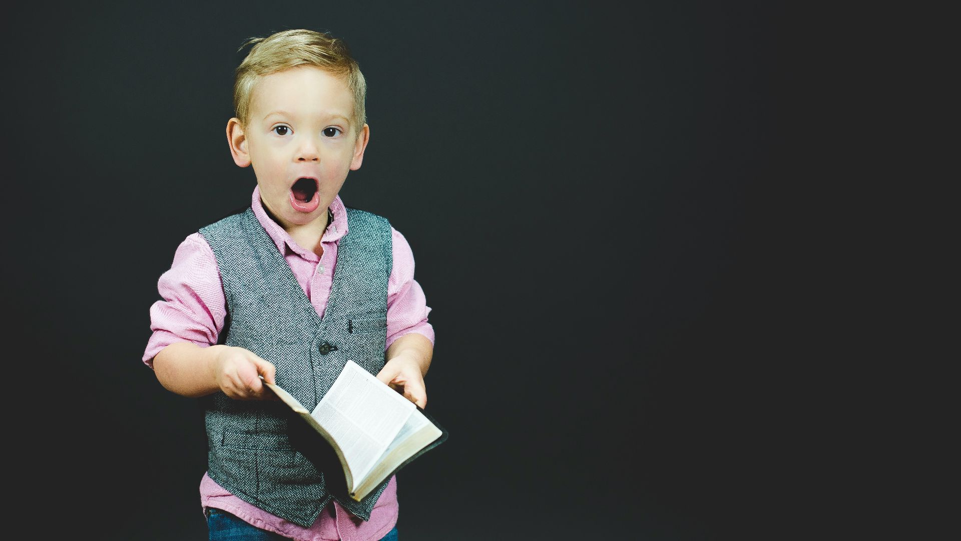 boy wearing gray vest and pink dress shirt holding book