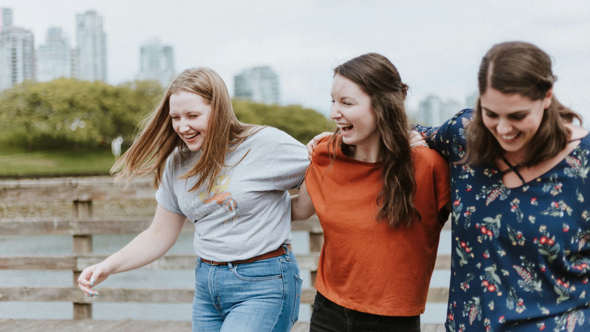 three women walking on brown wooden dock near high rise building during daytime