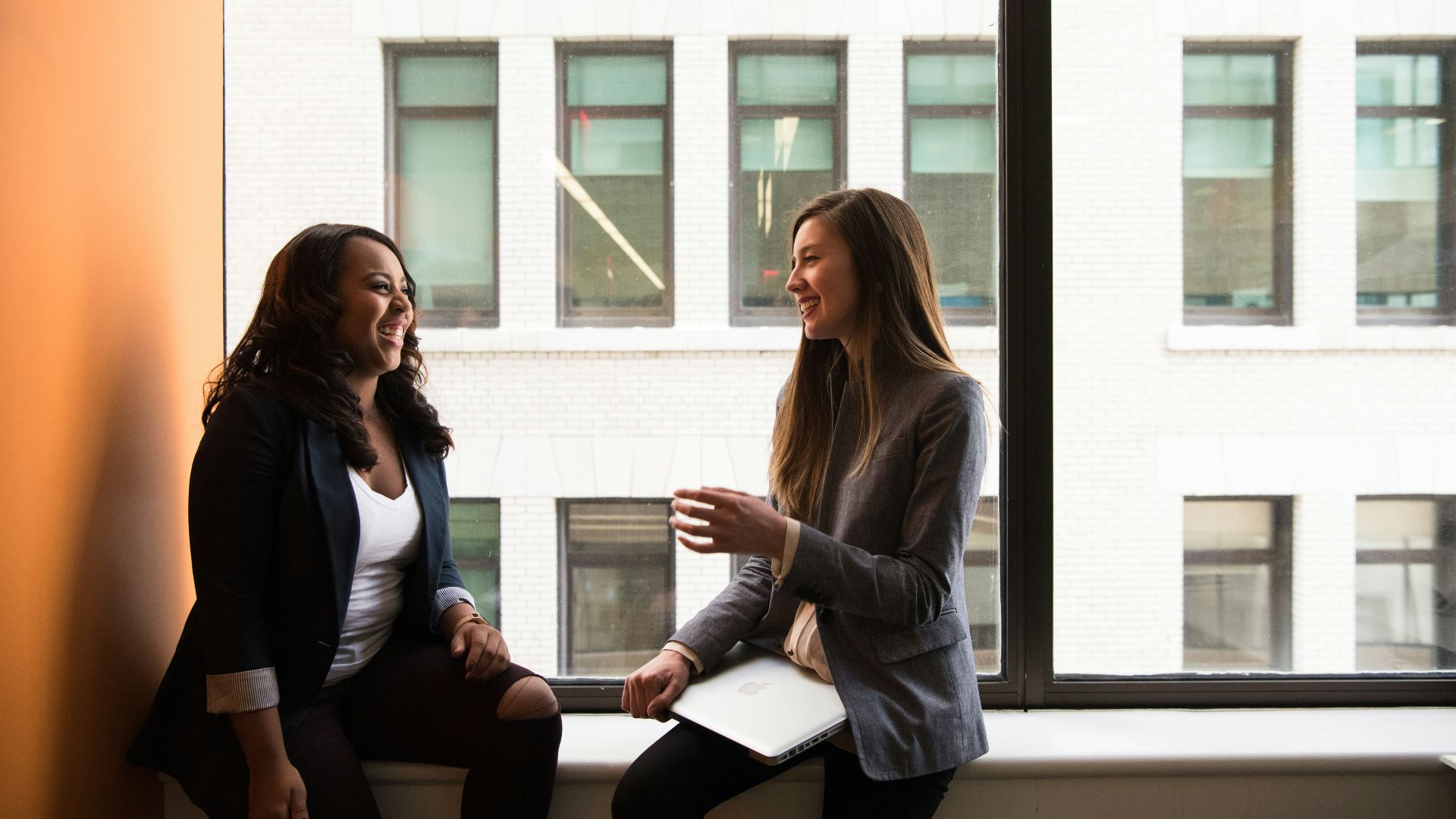 two woman sitting by the window laughing