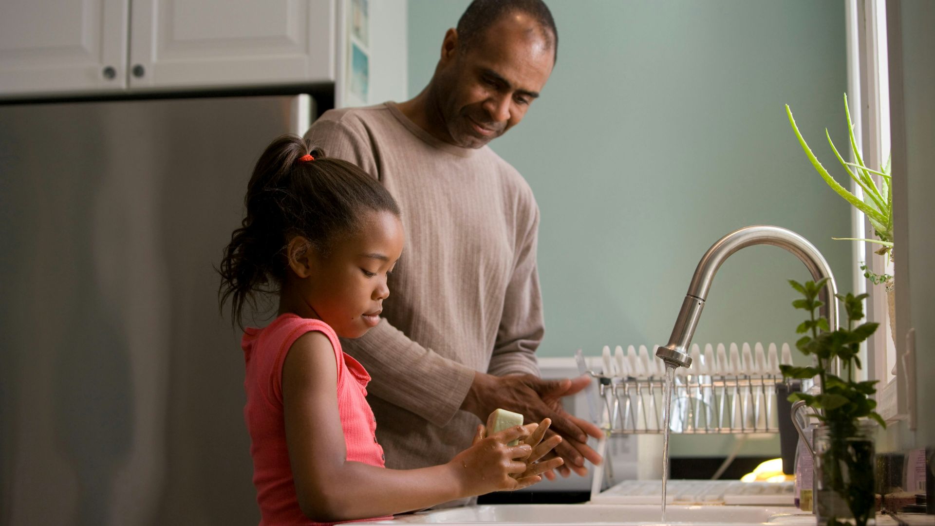 man in long sleeve shirt standing beside girl in pink tank top washing hands