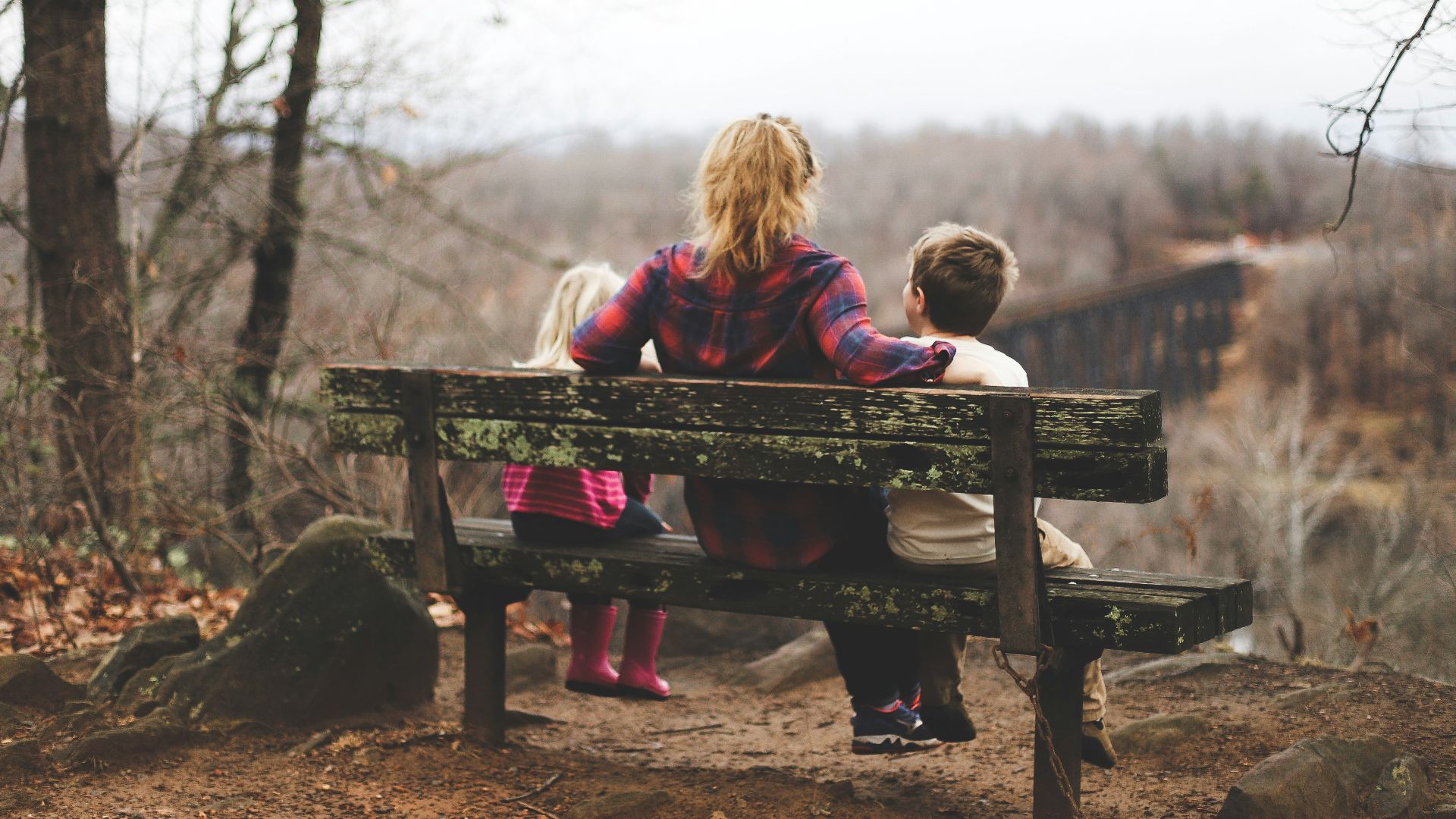 woman between two childrens sitting on brown wooden bench during daytime