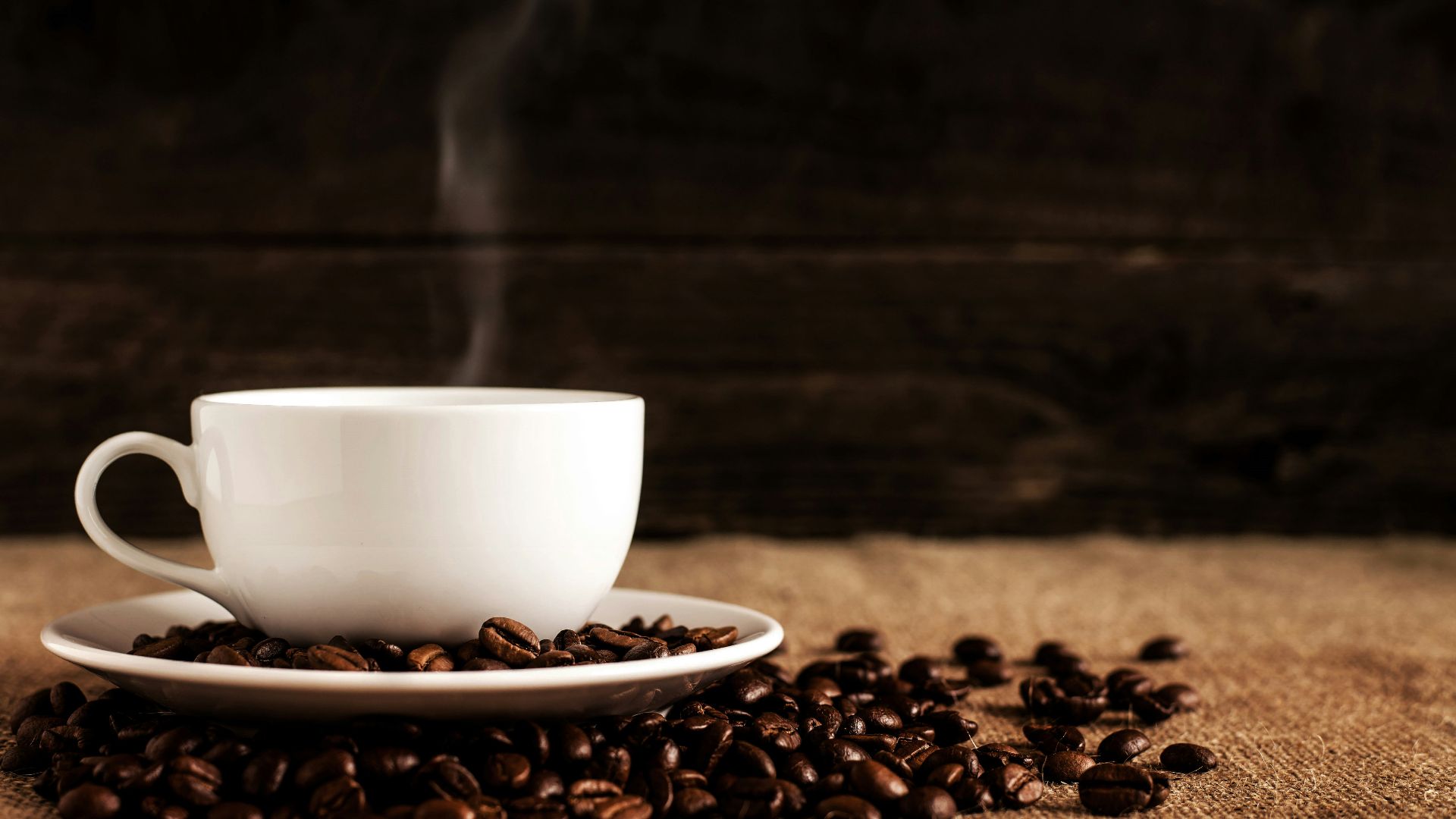 white ceramic mug and saucer with coffee beans on brown textile