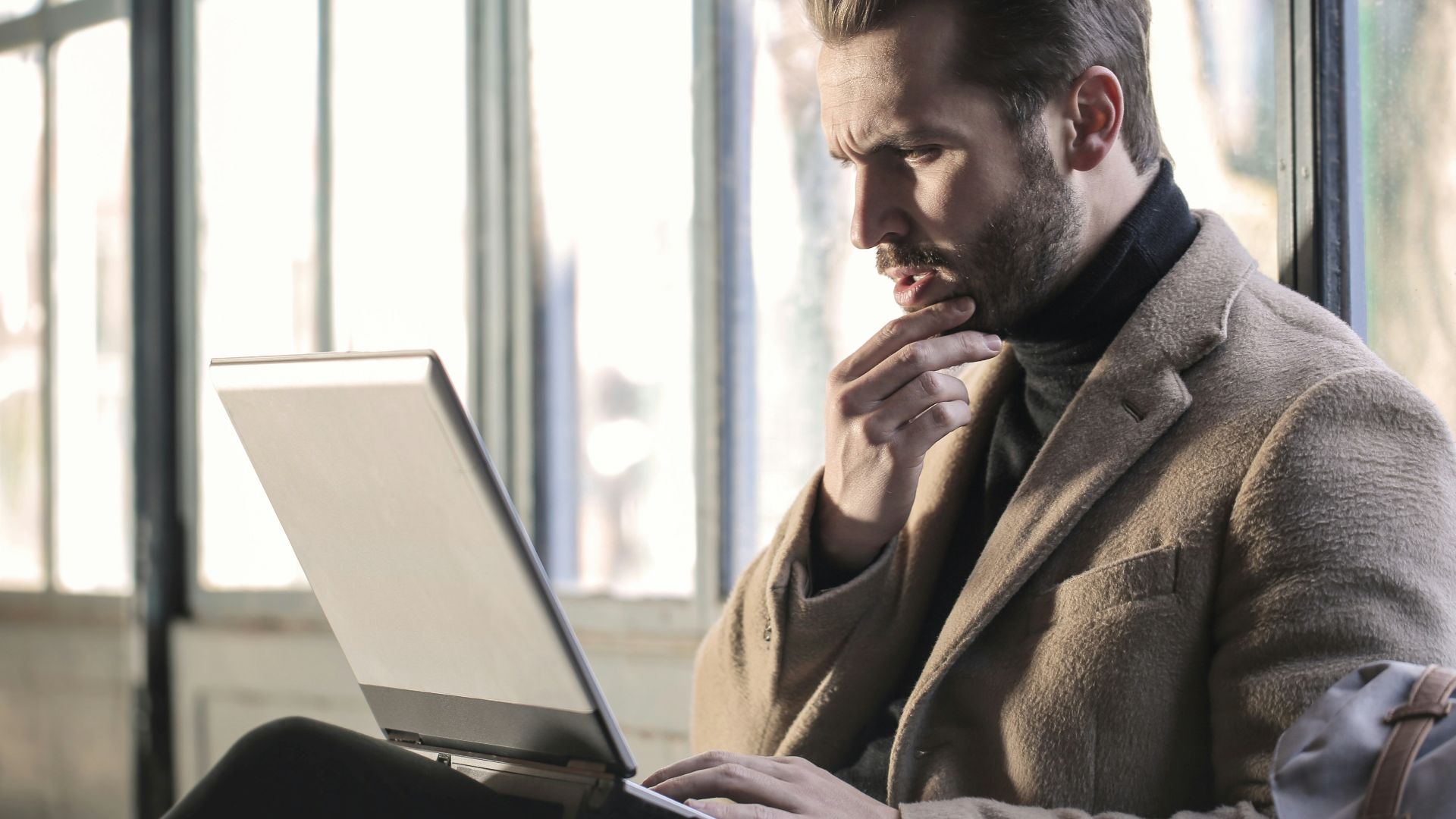 man holding his chin facing laptop computer