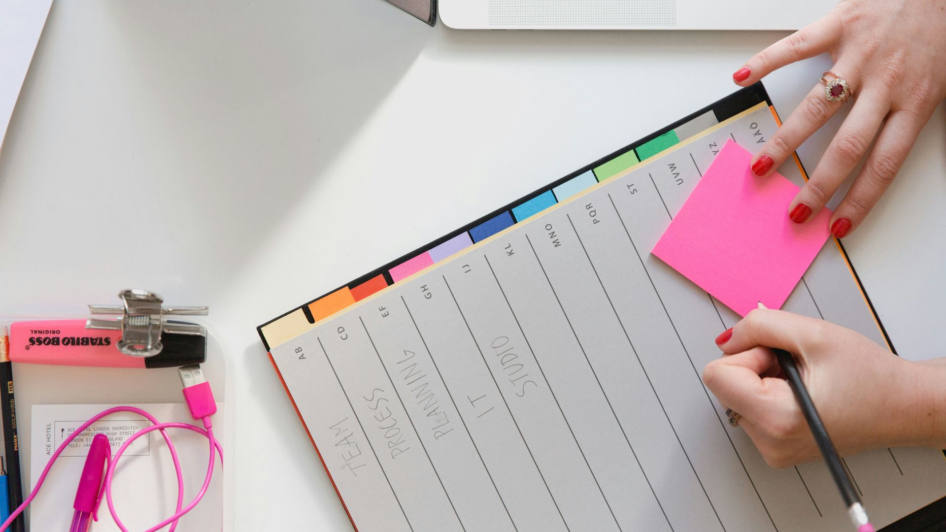 person holding pencil and stick note beside table