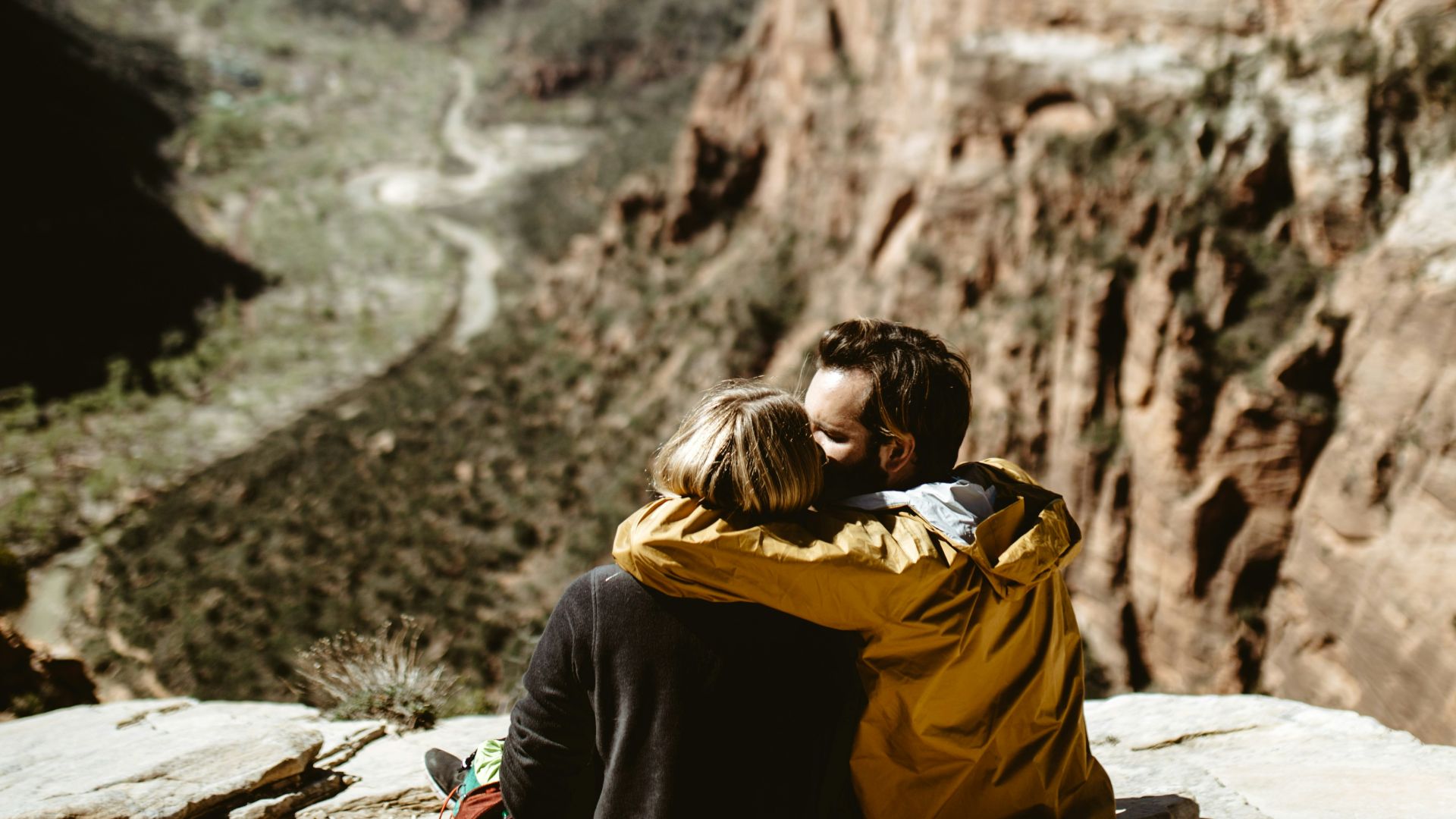 selective focus photography of couple sitting on rock fall under sunlight