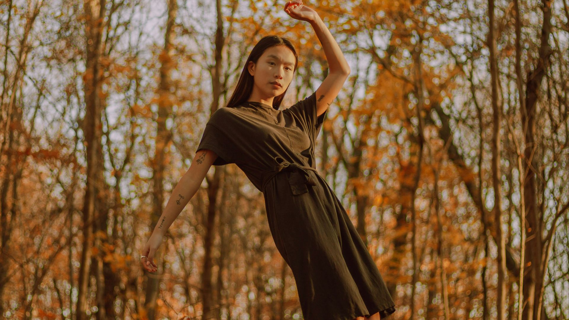 woman in black dress standing near brown trees during daytime