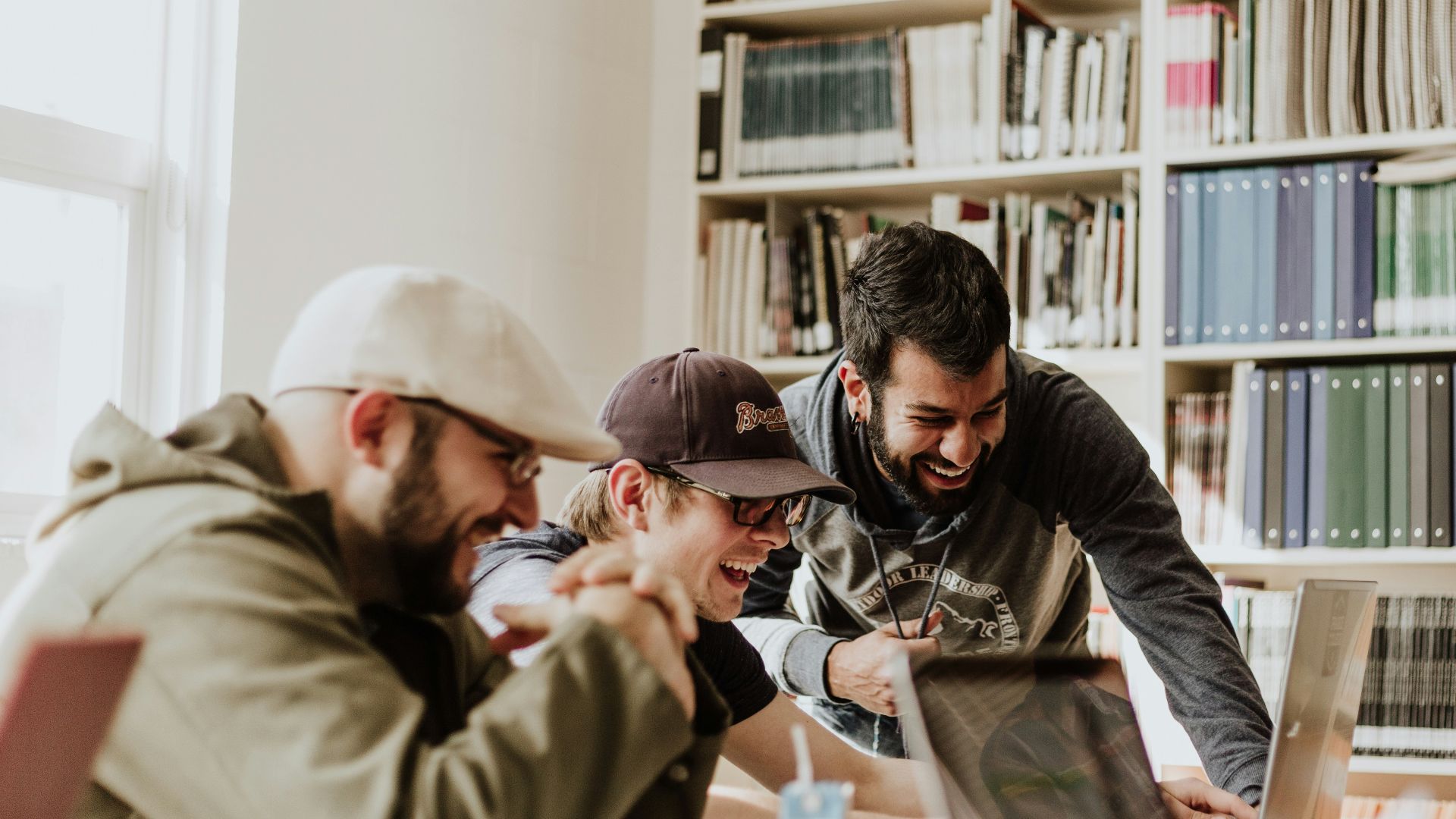 three men laughing while looking in the laptop inside room