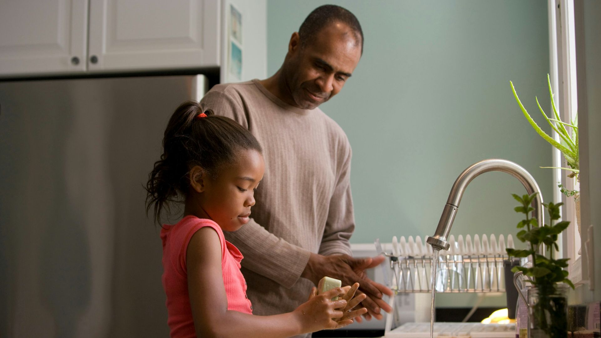 man in long sleeve shirt standing beside girl in pink tank top washing hands