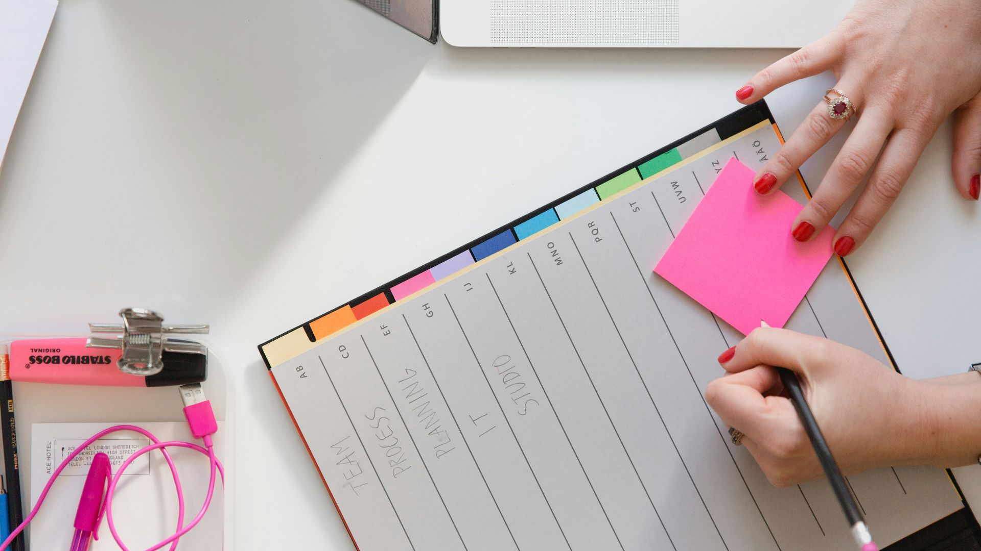 person holding pencil and stick note beside table