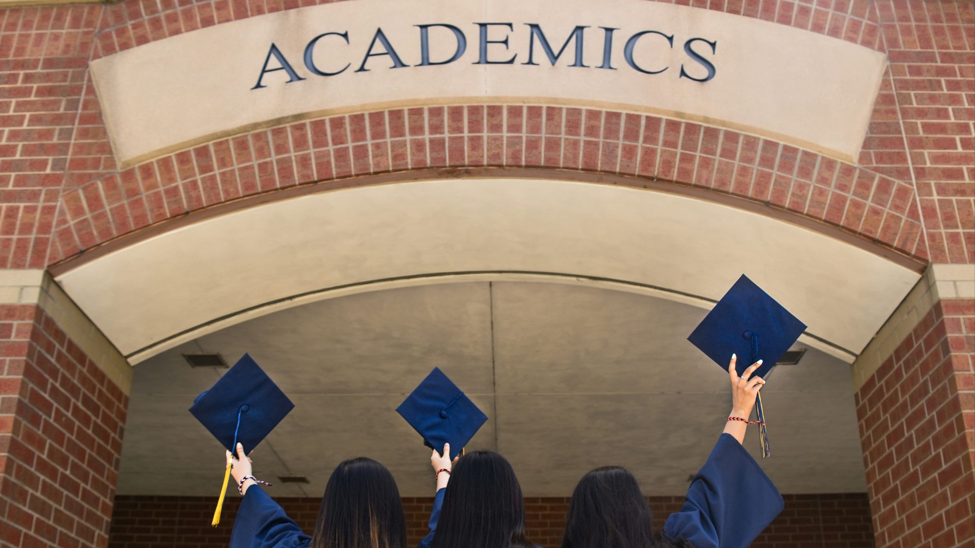 three girls in graduation gowns hold their caps in the air