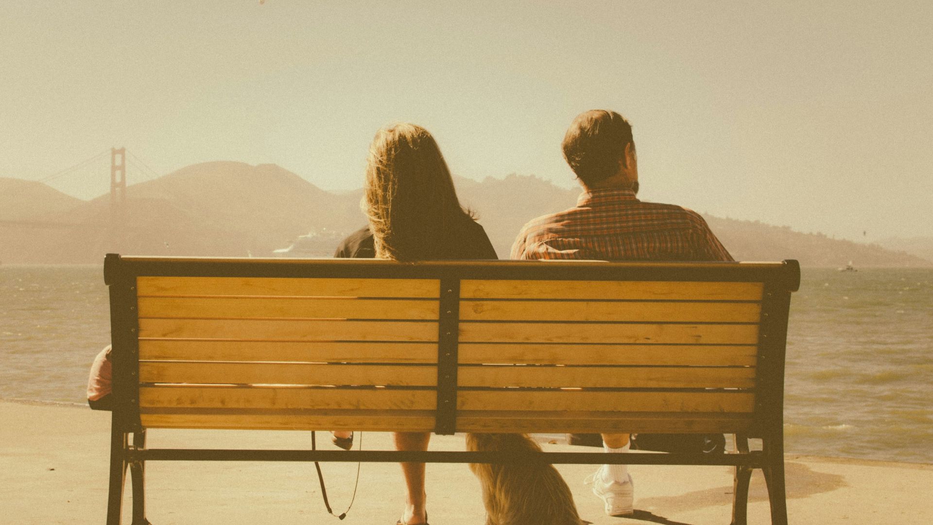 man and woman sitting on bench beside body of water