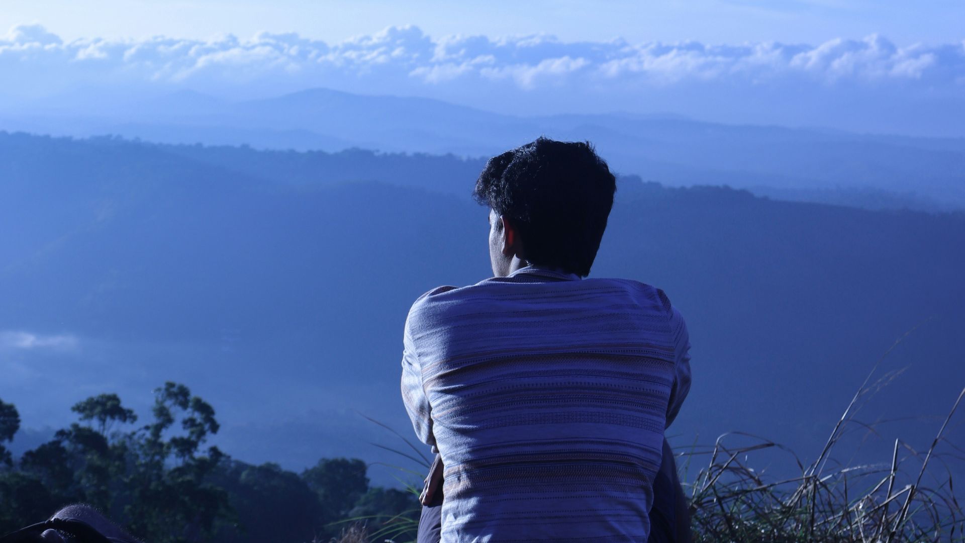 man in white shirt sitting on rock looking at mountains during daytime