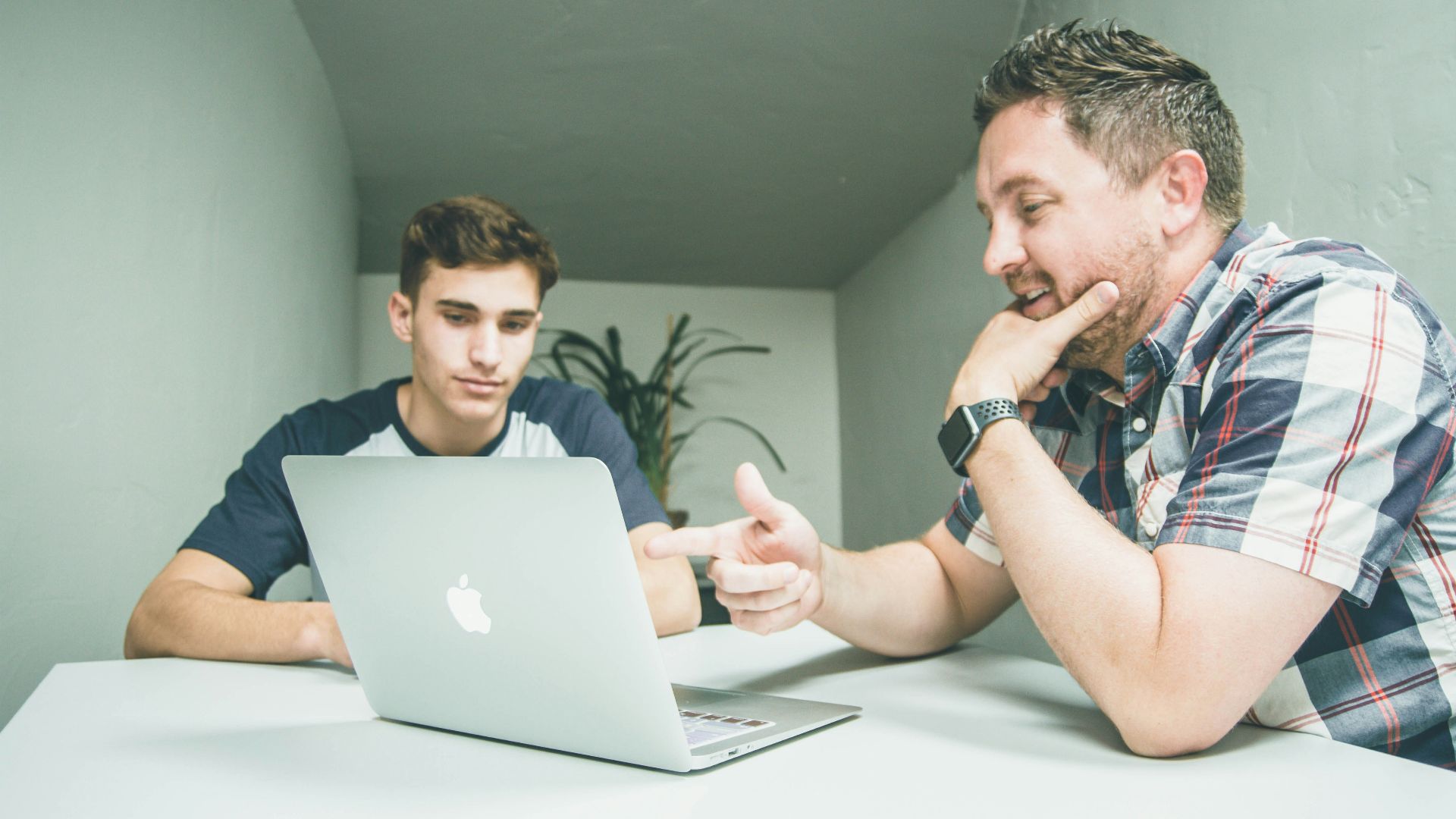 man wearing white and black plaid button-up sports shirt pointing the silver MacBook