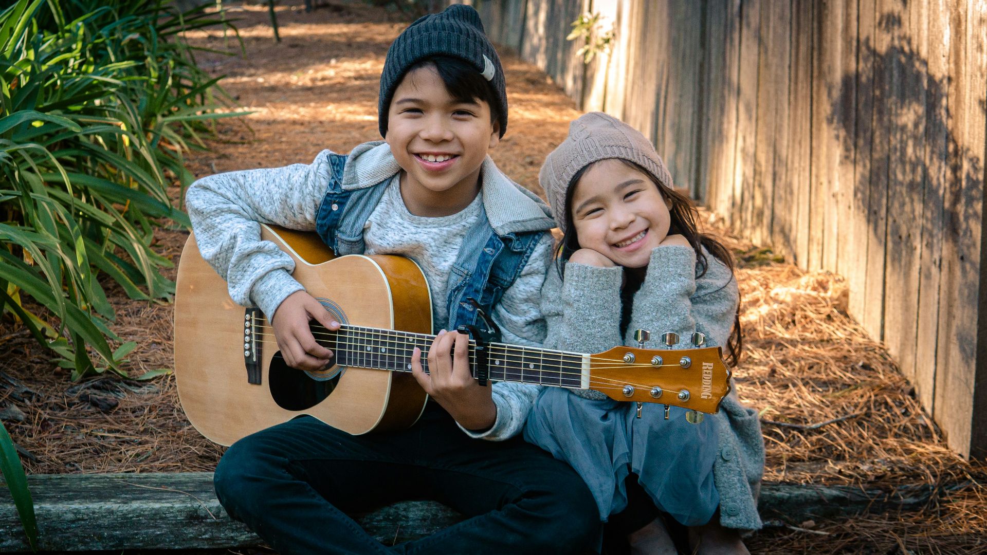 boy holding dreadnought acoustic guitar beside girl during daytime