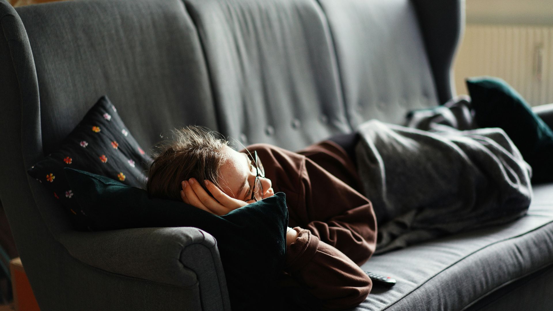 woman in pink jacket lying on gray couch