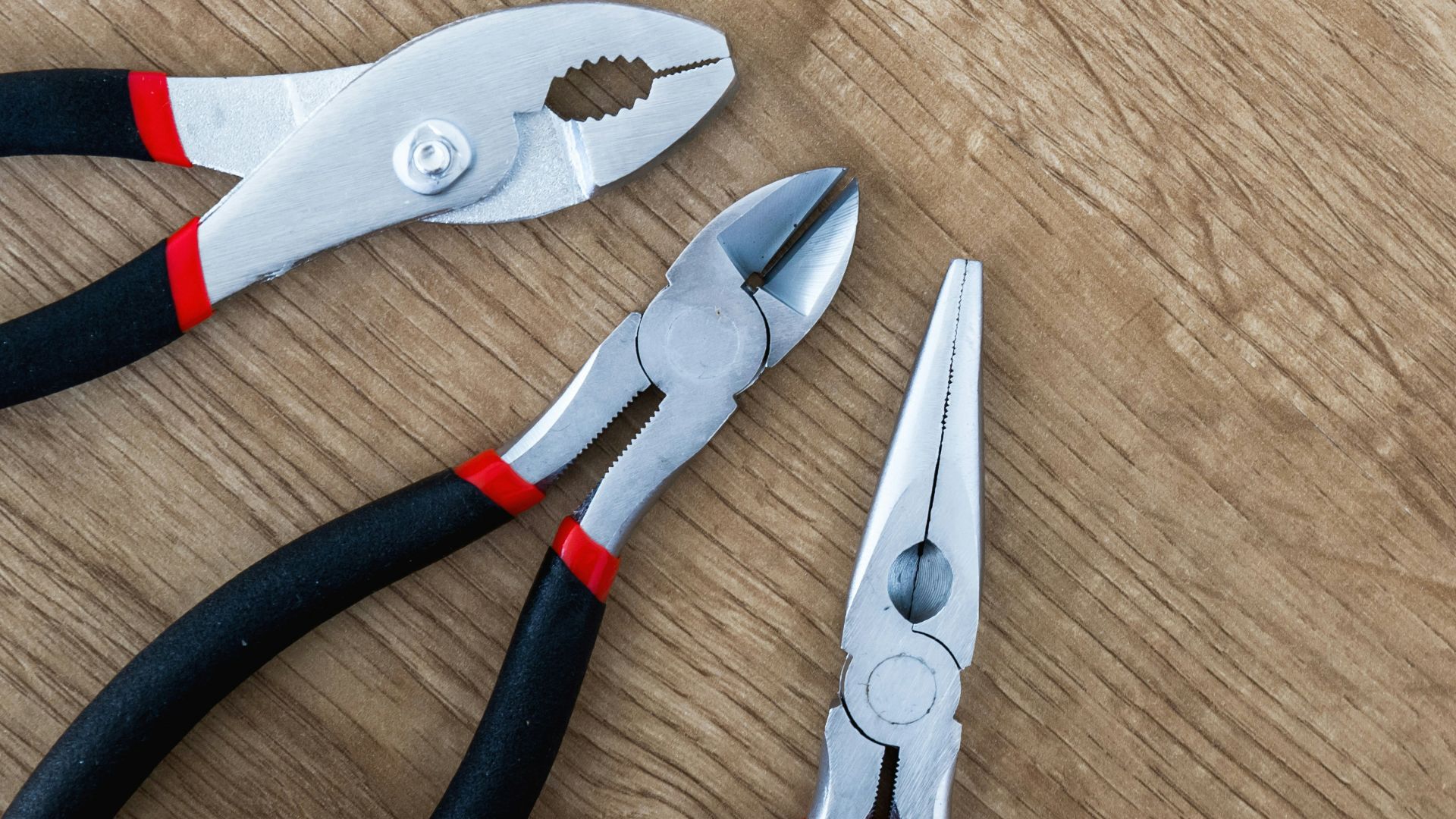 three black handled pliers on brown surface