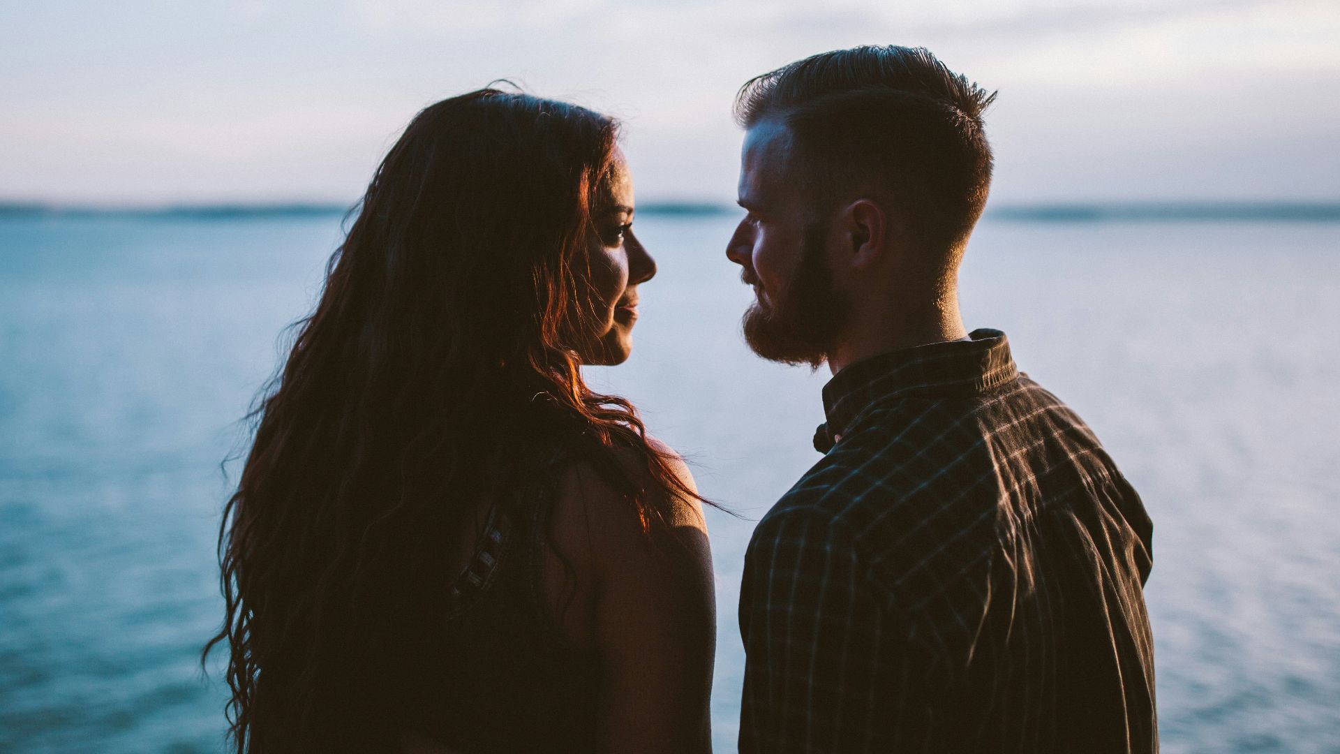 man and woman standing while looking each other near body of water