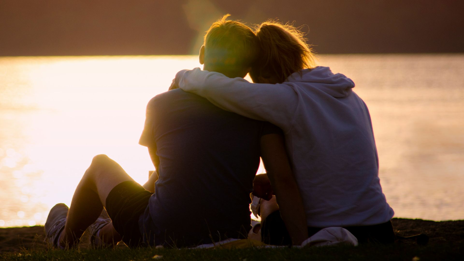 woman in black jacket sitting on green grass field near body of water during daytime