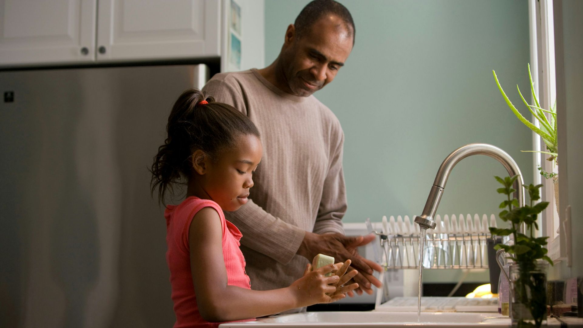 man in long sleeve shirt standing beside girl in pink tank top washing hands