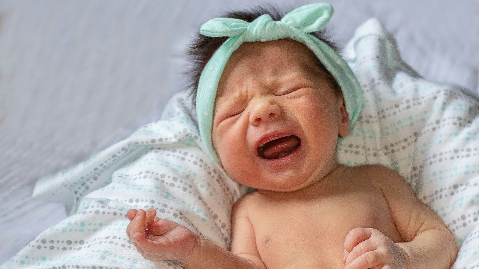 a baby crying while laying on a bed