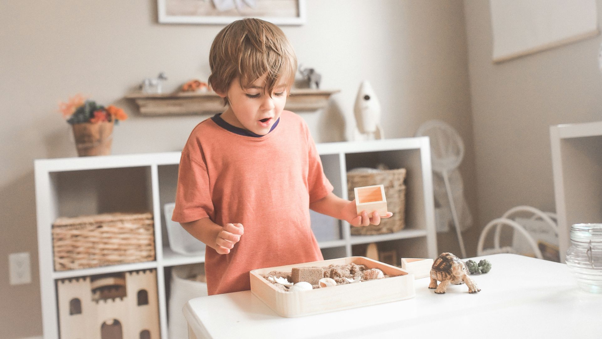 boy in orange crew neck t-shirt standing in front of white wooden table with cupcakes